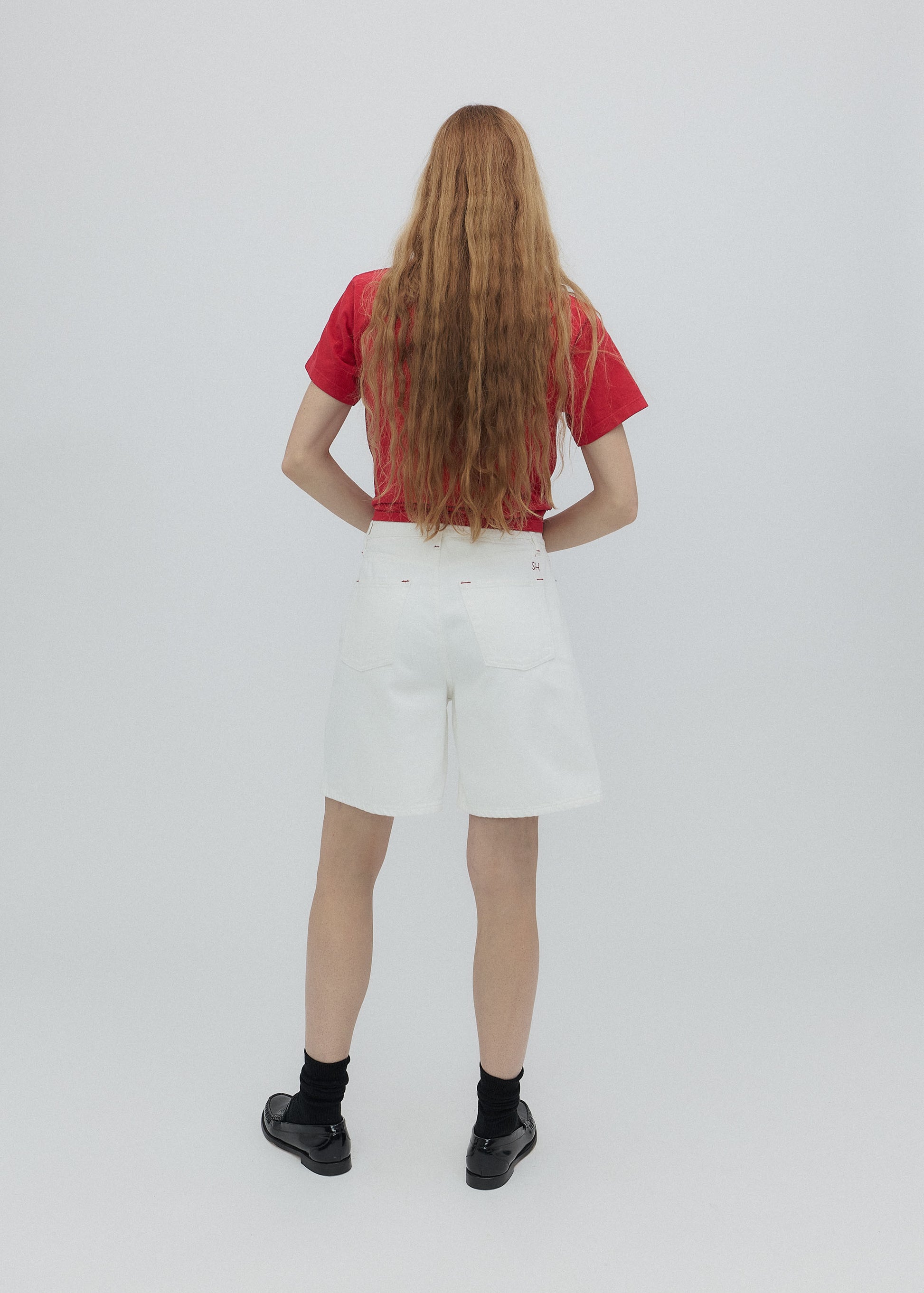 Person wearing a red shirt and white shorts from behind on a plain background