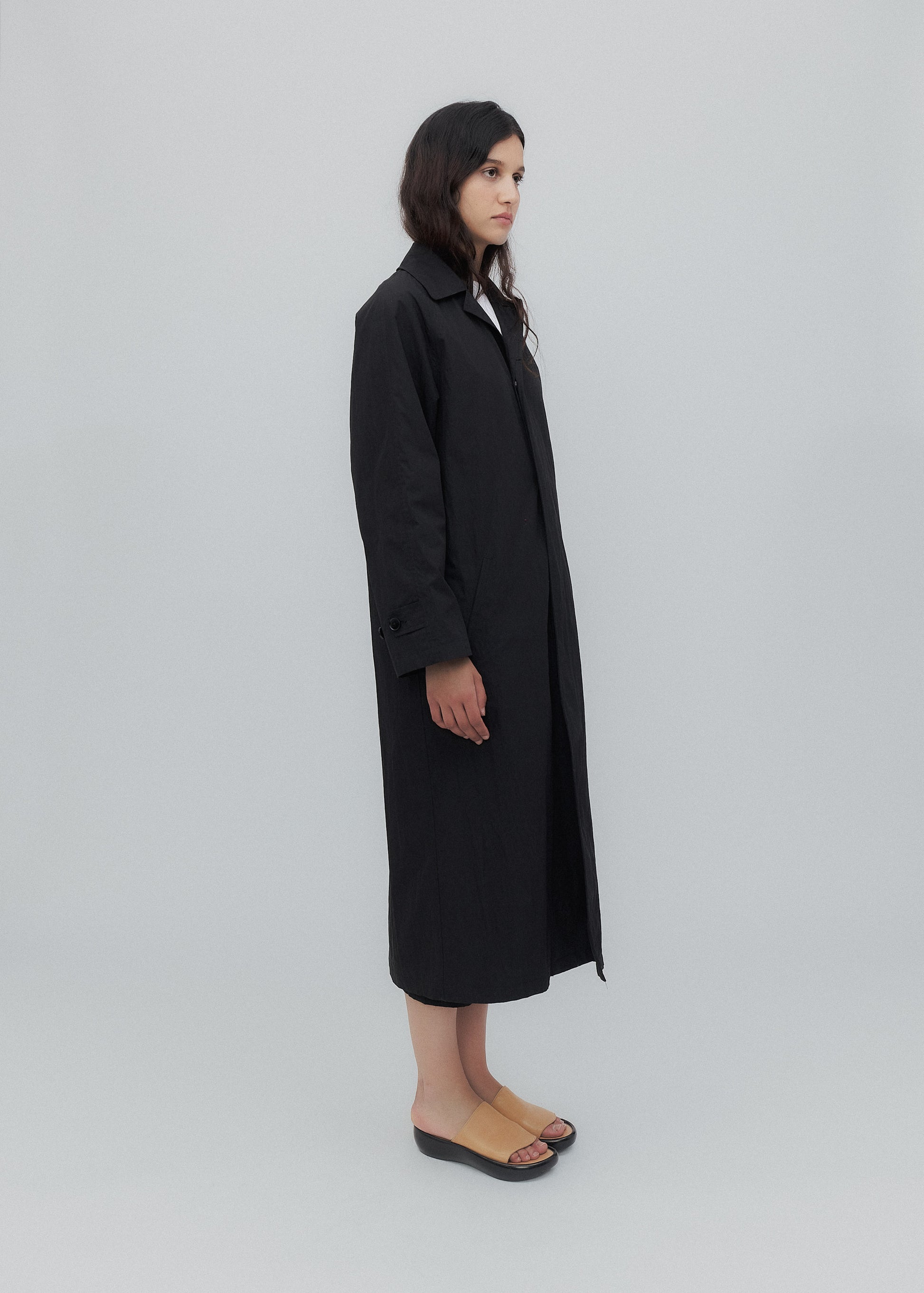 Person wearing a long black coat on a light gray background