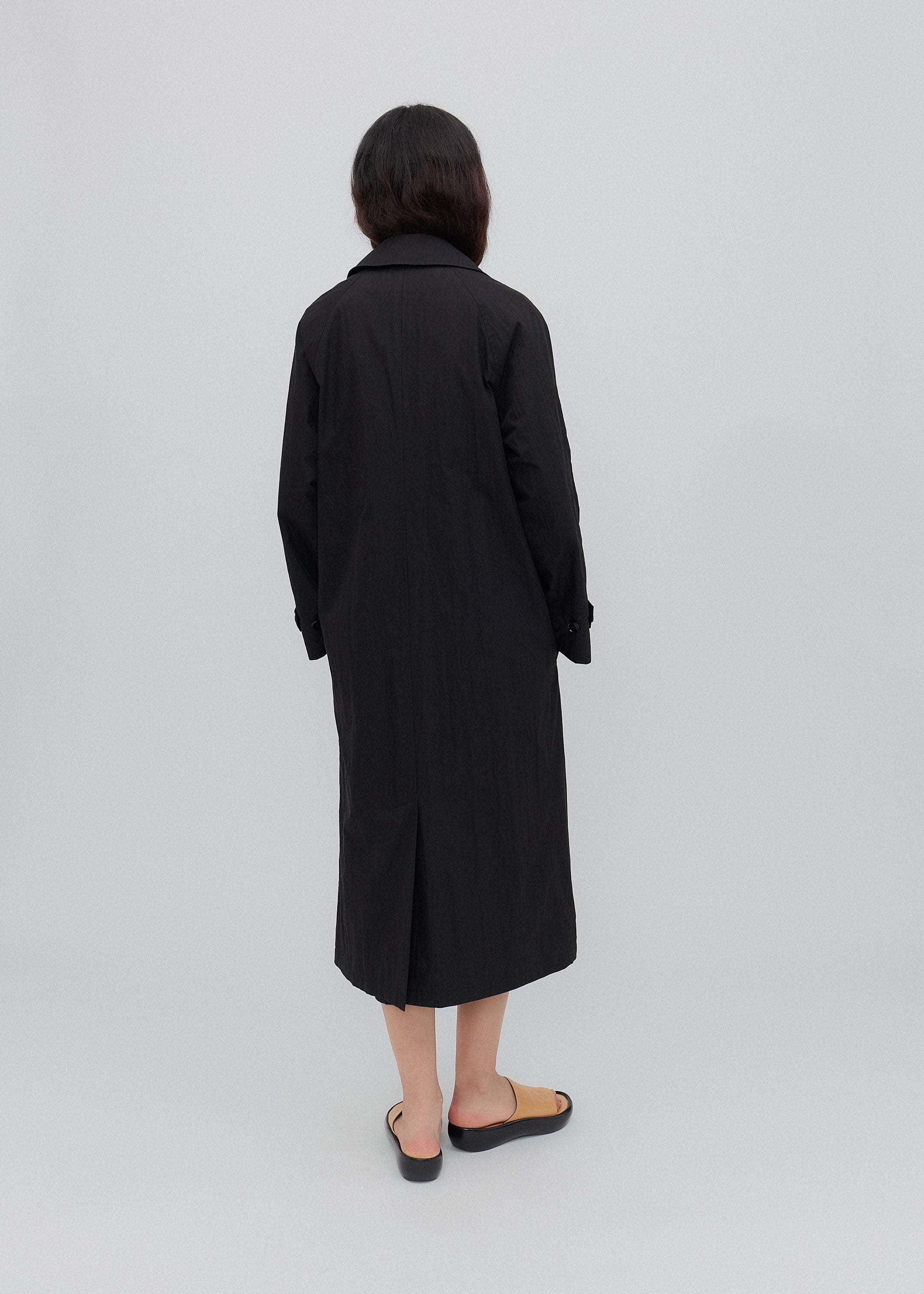 Person wearing a black coat standing against a white background