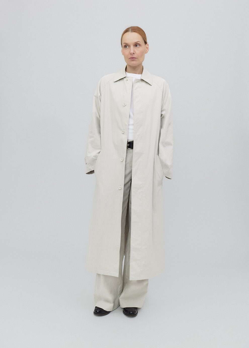 Person wearing a long white coat on a light gray background