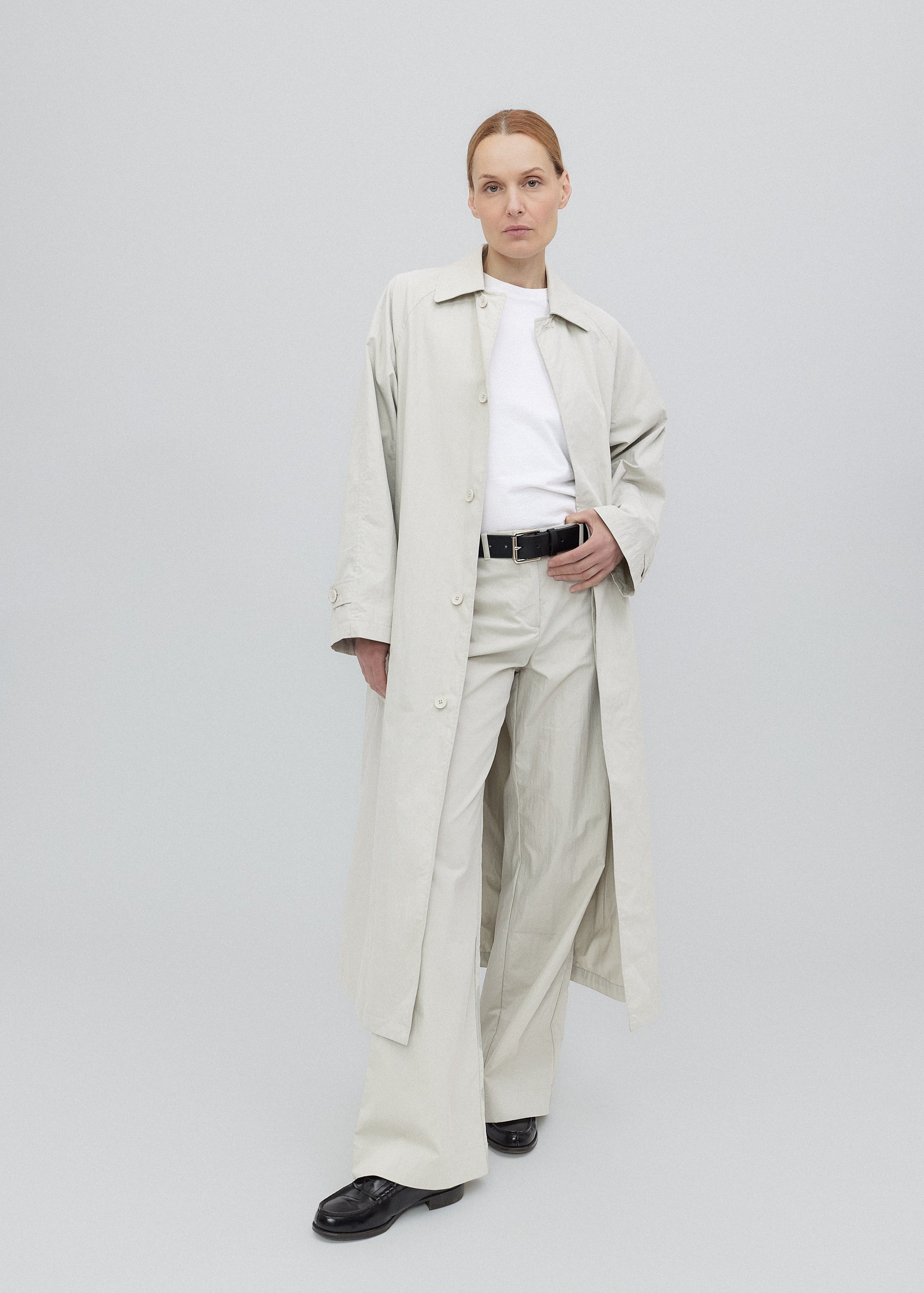 Person wearing a long beige trench coat on a plain background