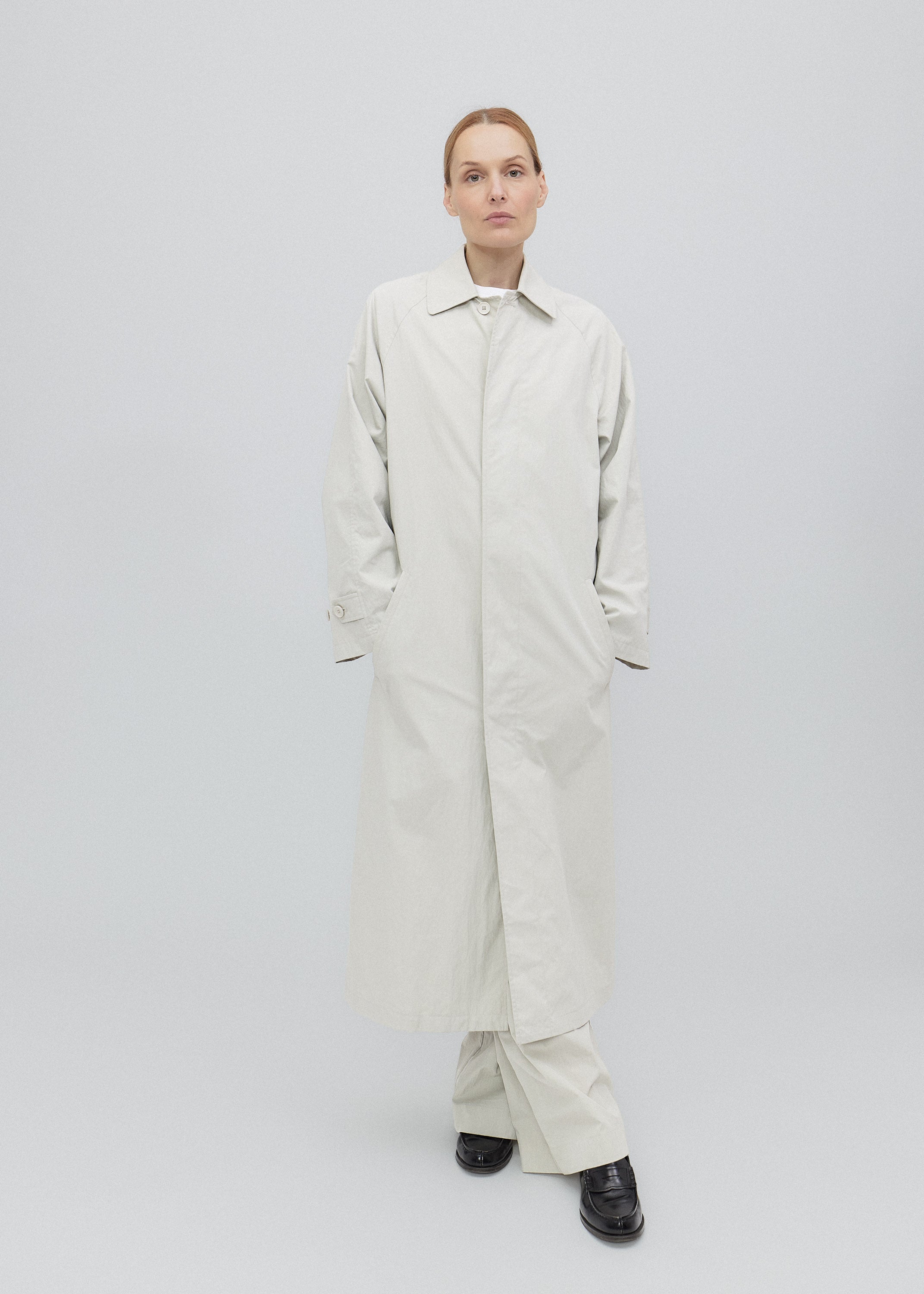 Person wearing a long beige coat on a plain background
