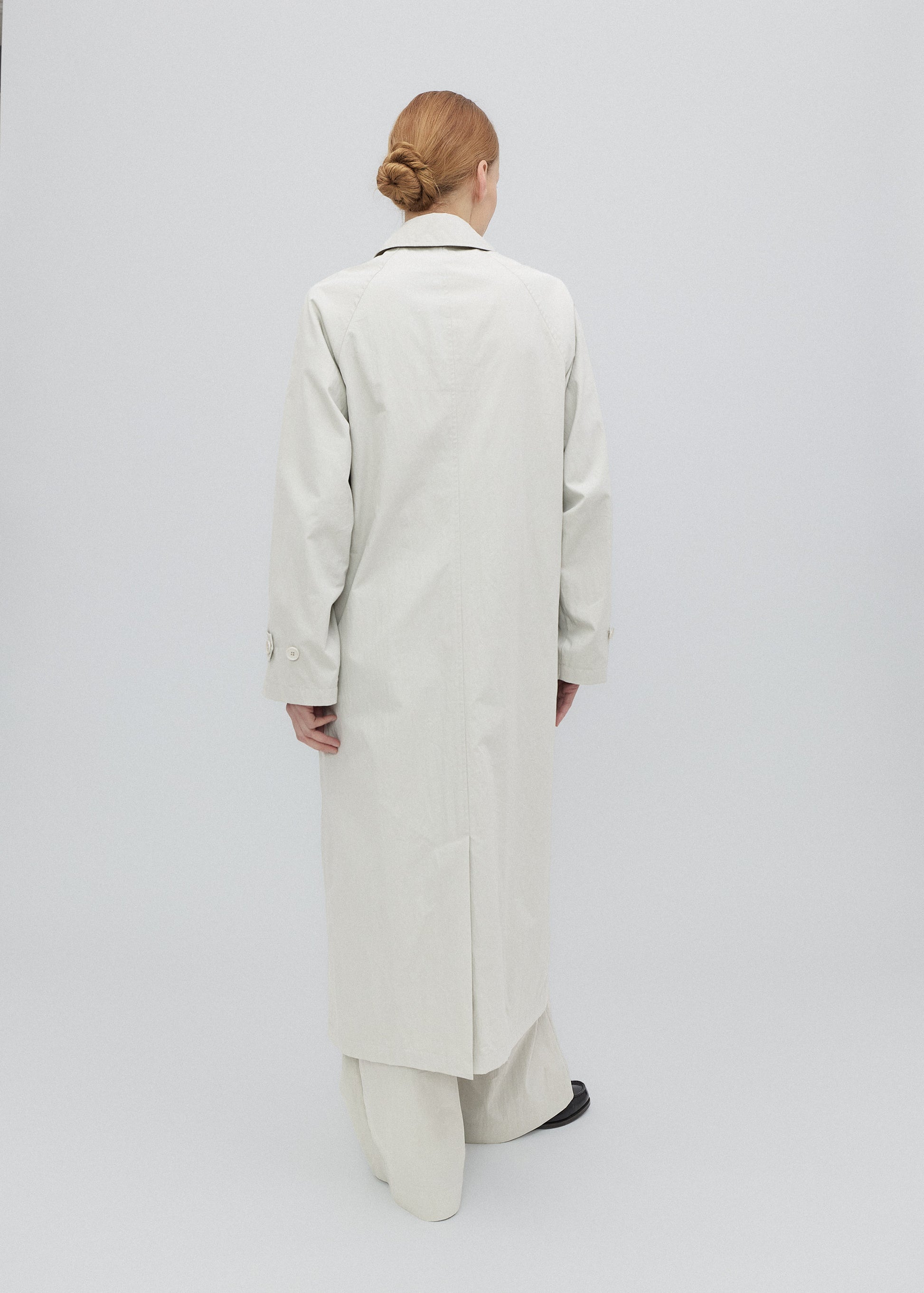 Person wearing a long beige coat on a white background