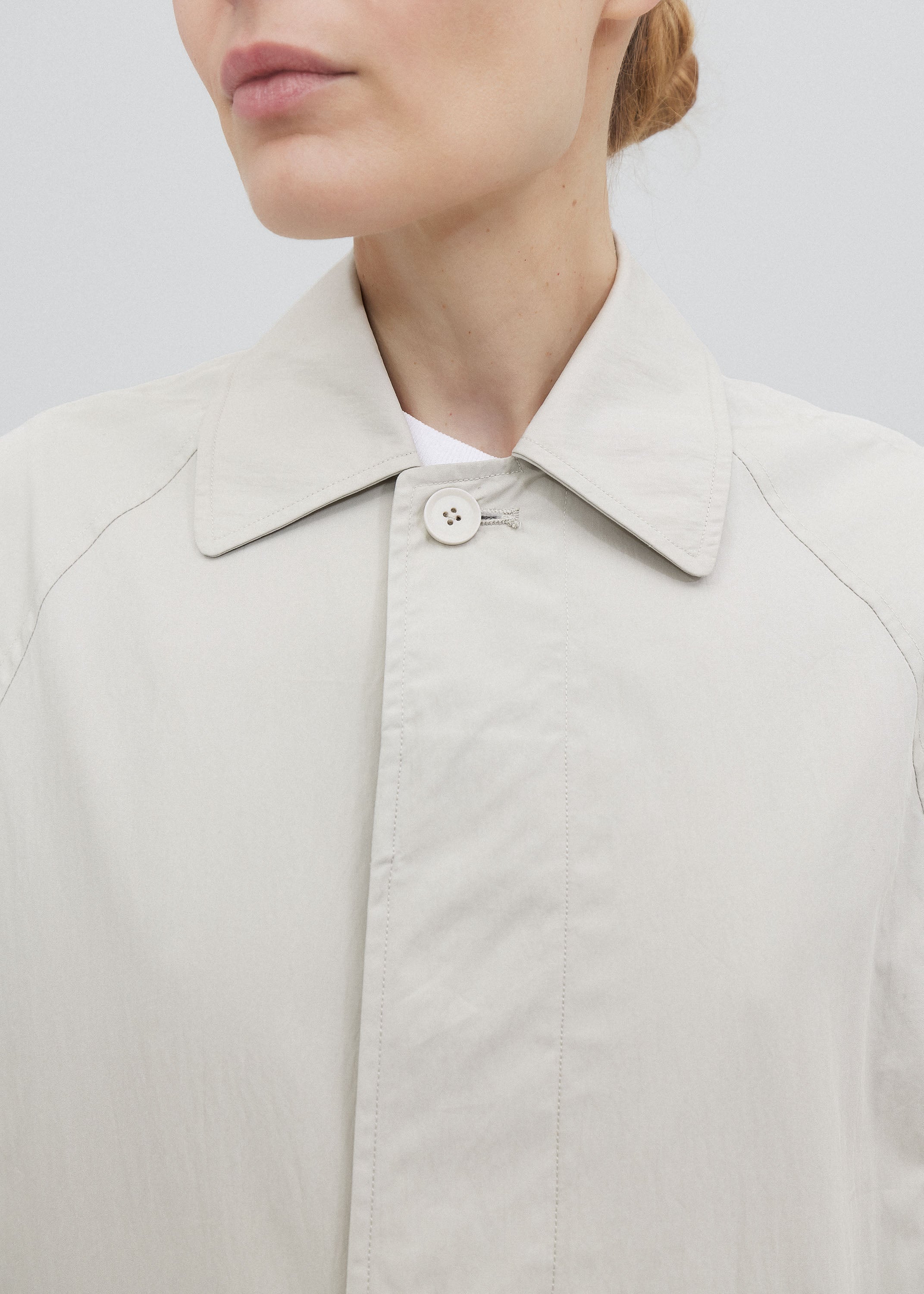 Close-up of a person wearing a light gray coat with a button on a plain background