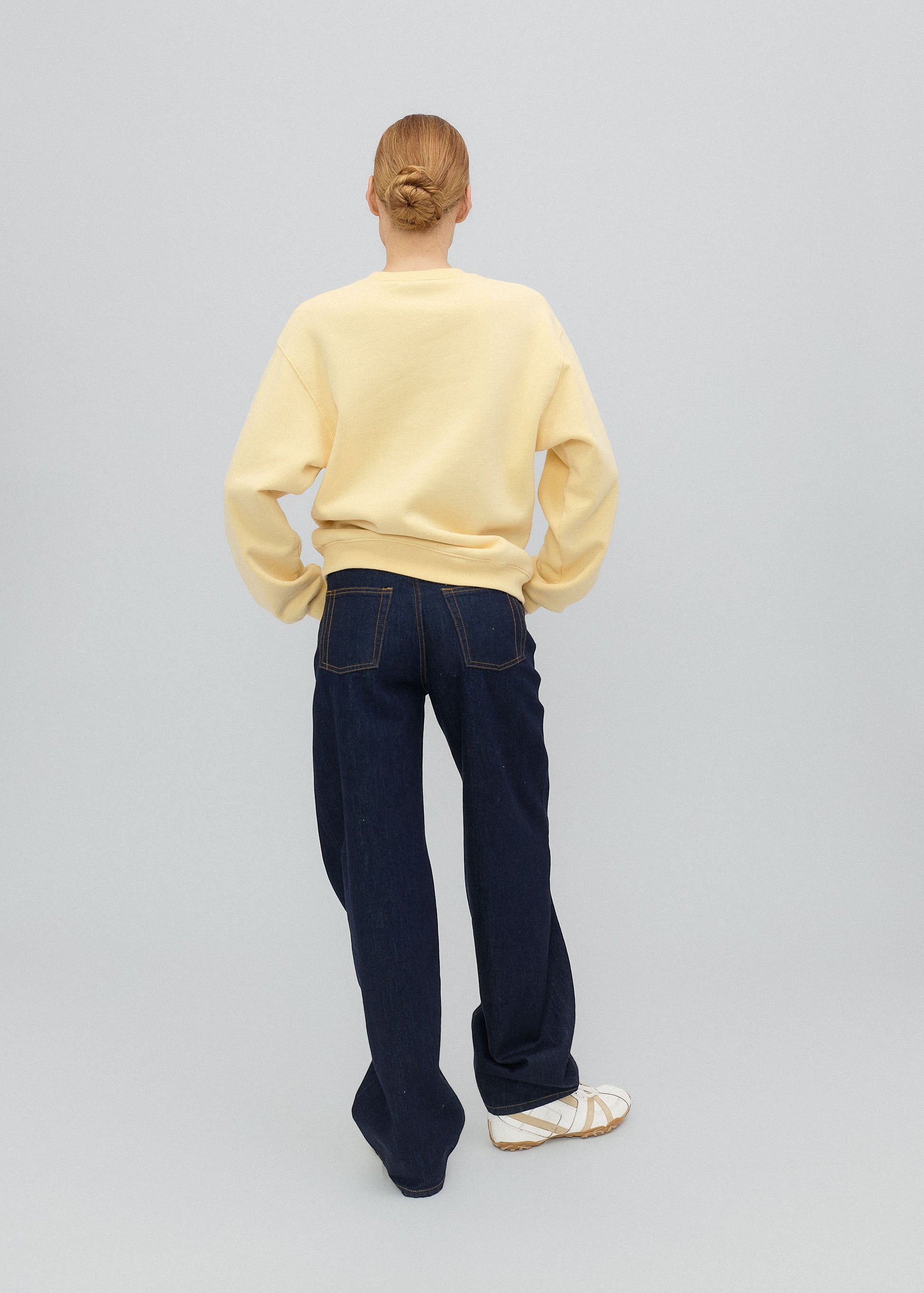 Person wearing a yellow sweater and dark blue jeans on a light gray background