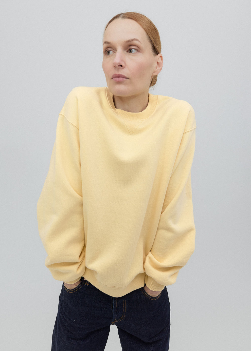 Person wearing a light yellow sweater and dark pants on a plain background