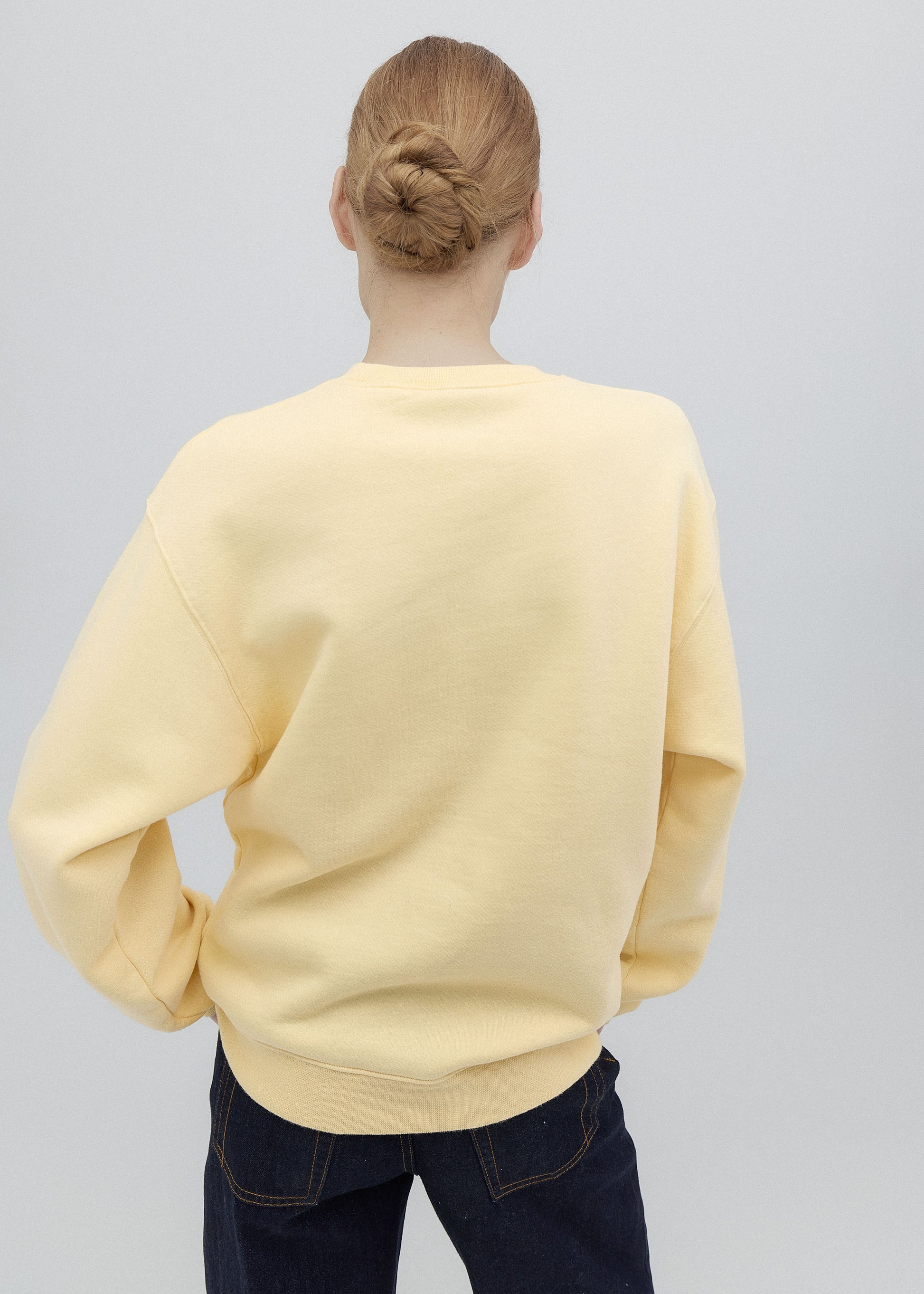 Person wearing a light yellow sweater and dark jeans on a plain background