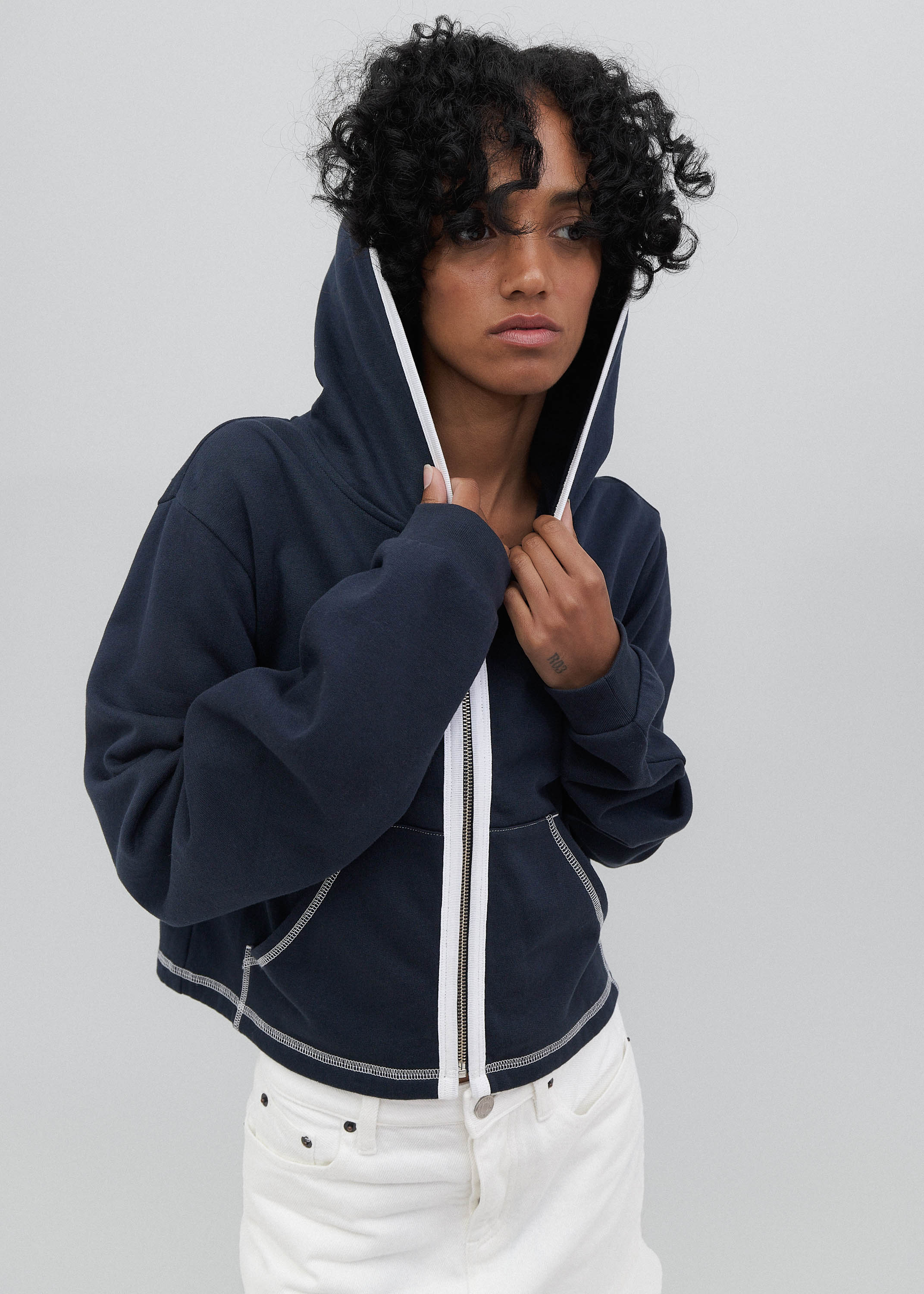 Person wearing a navy blue hoodie with white drawstrings on a light gray background