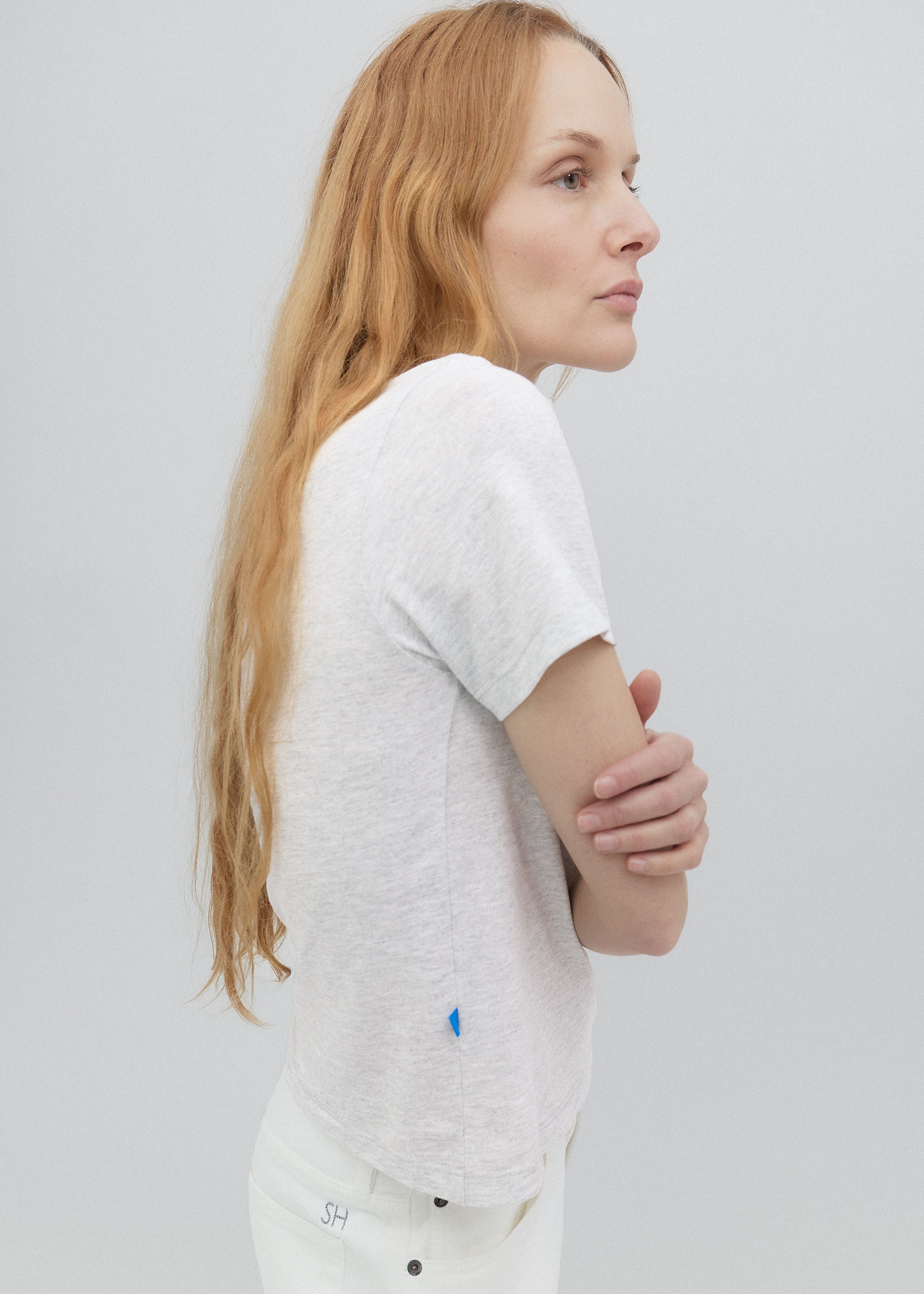 Woman wearing a white t-shirt with a small logo on a plain background