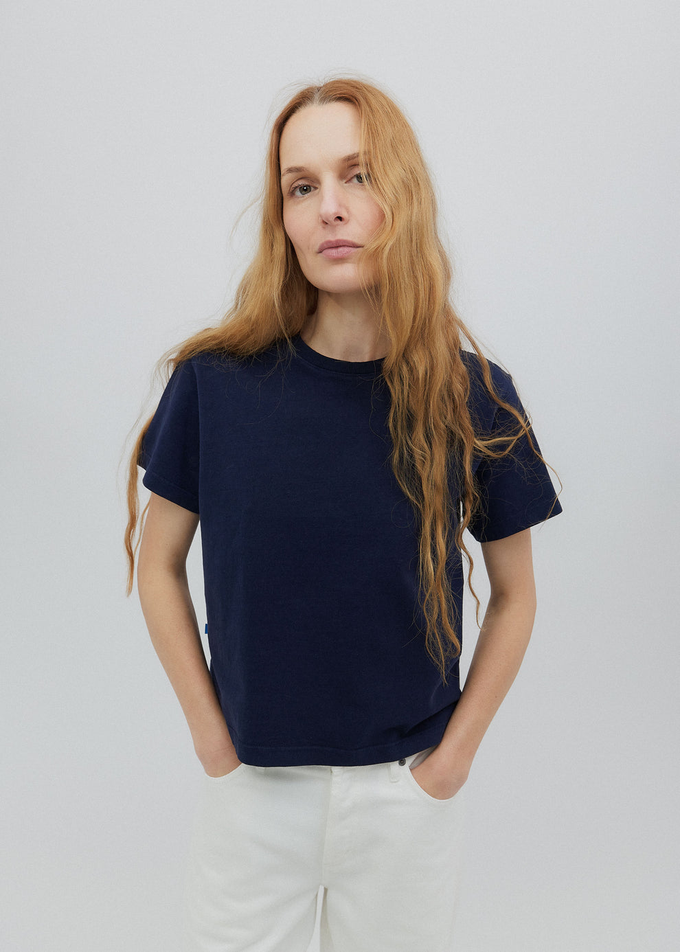 Woman wearing a navy blue t-shirt and white pants against a plain background