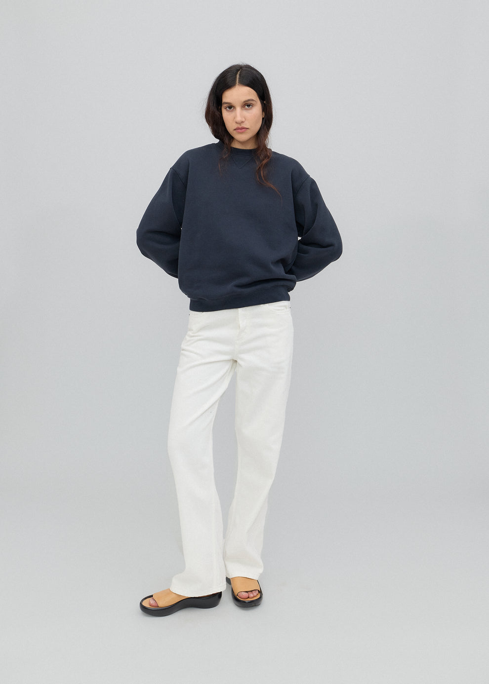 Person wearing a navy blue sweater and white jeans on a white background