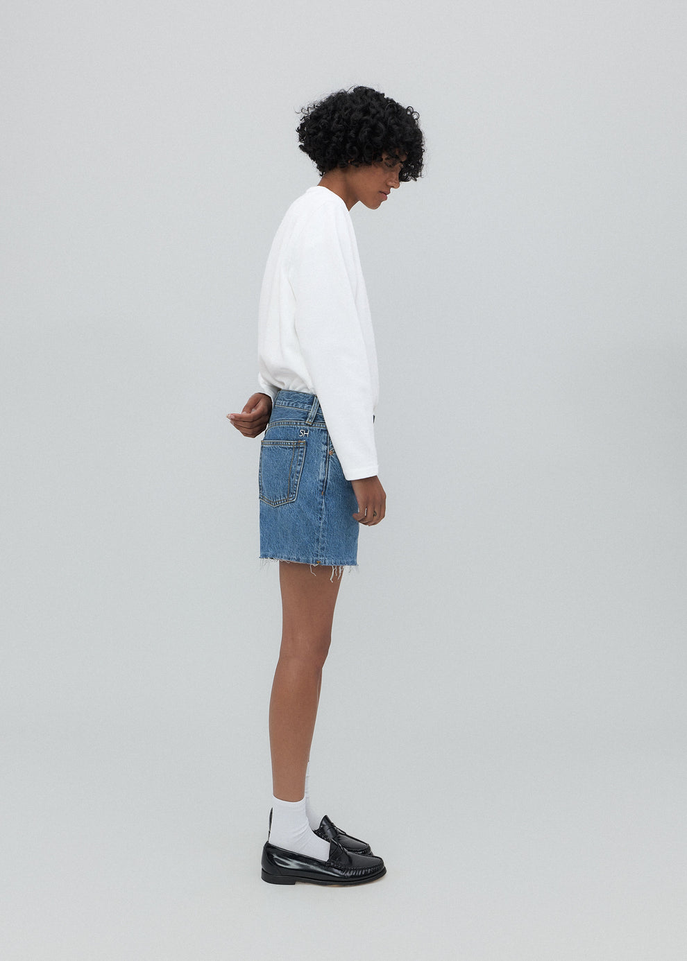 Person wearing a white sweater and denim skirt on a plain background