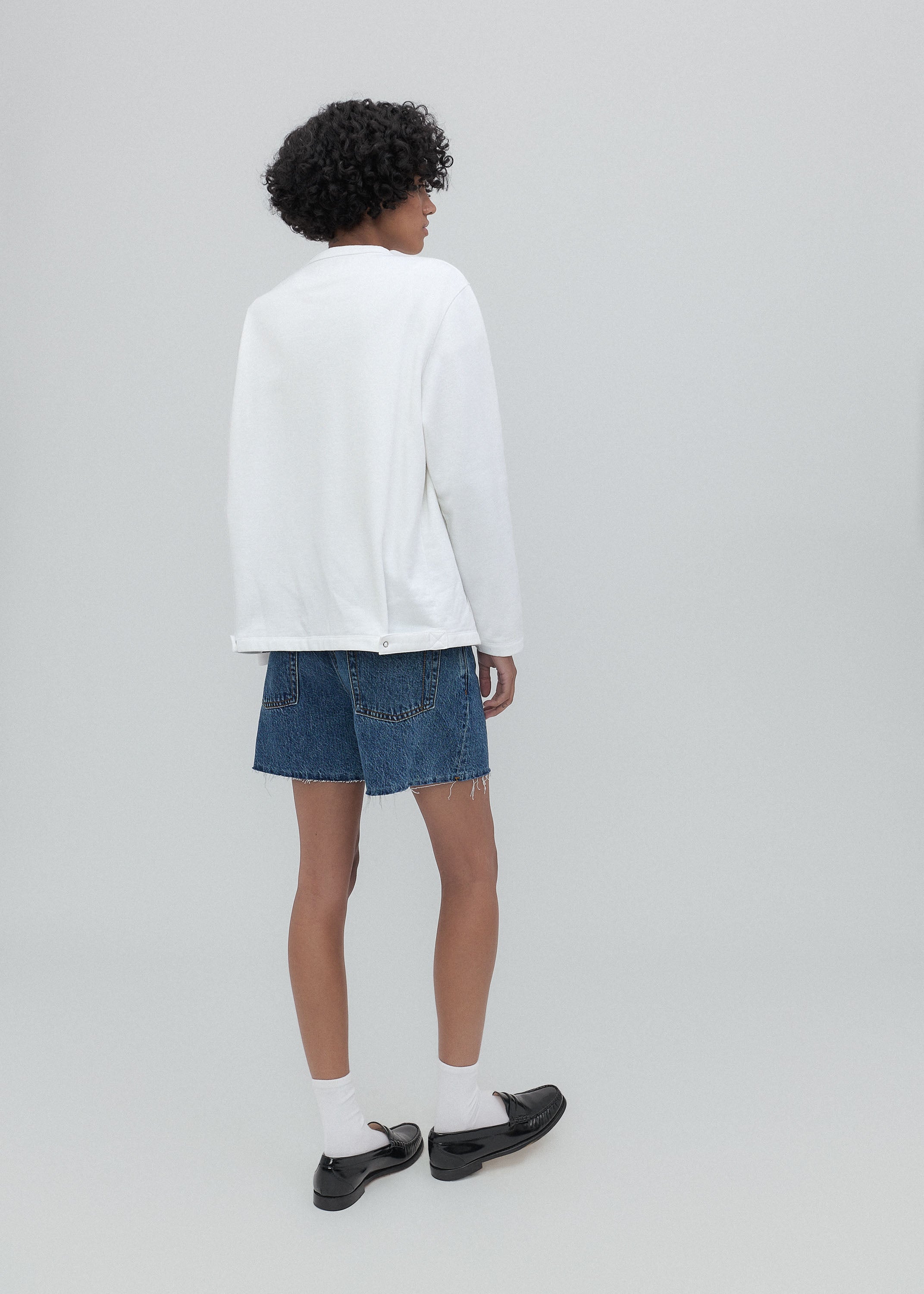 Person wearing a white sweatshirt and blue denim shorts on a plain background