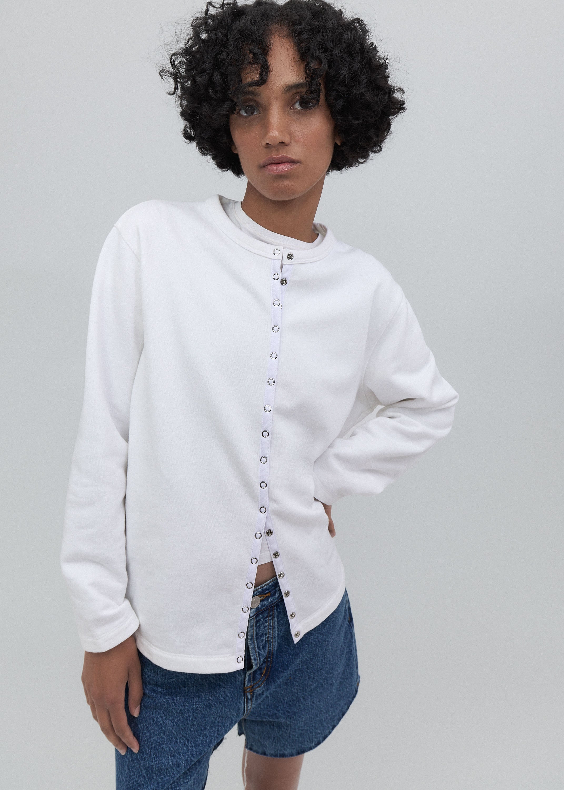 Person wearing a white button-up shirt and blue jeans against a gray background