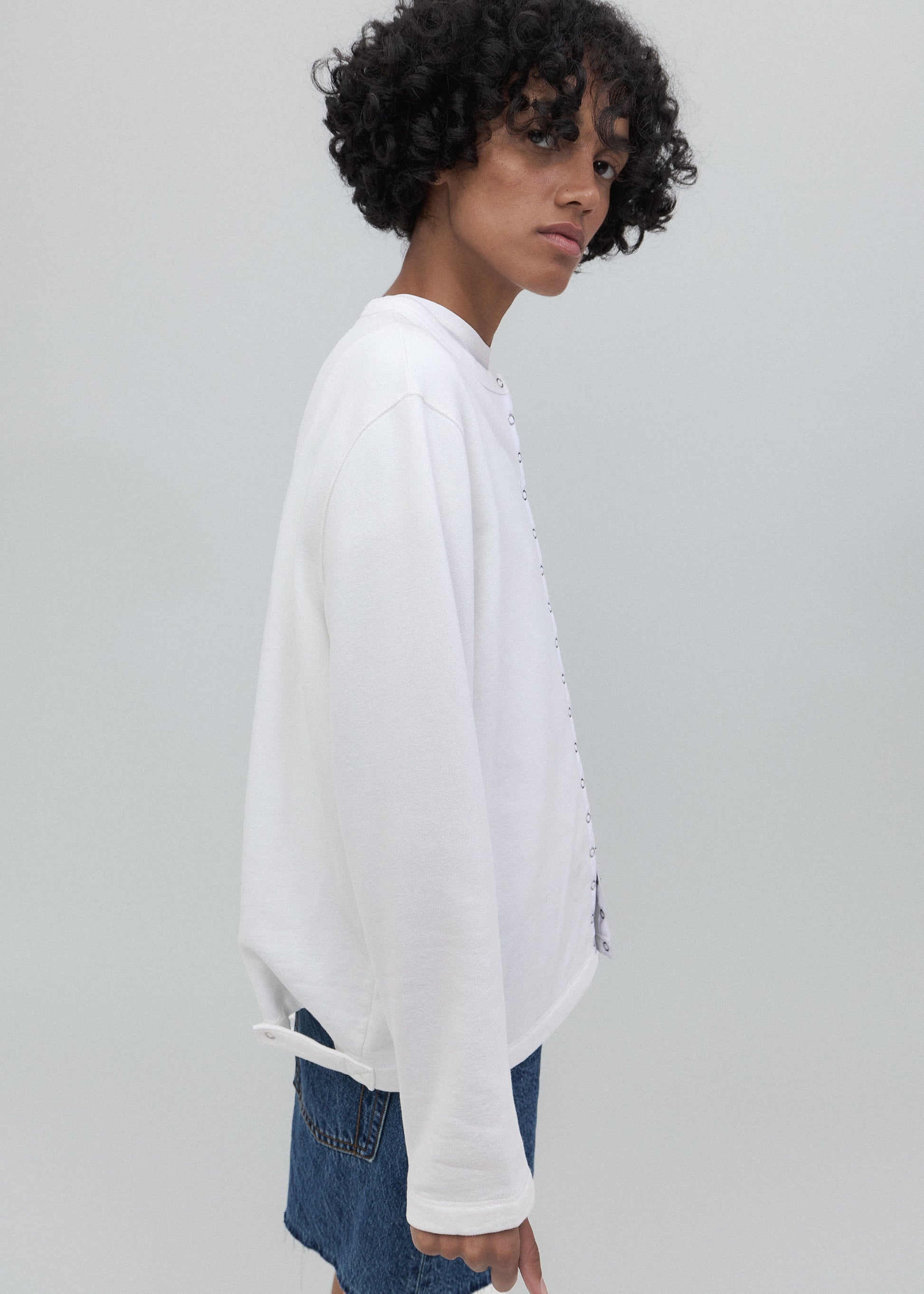 Person wearing a white oversized sweatshirt with a brand logo on a light gray background
