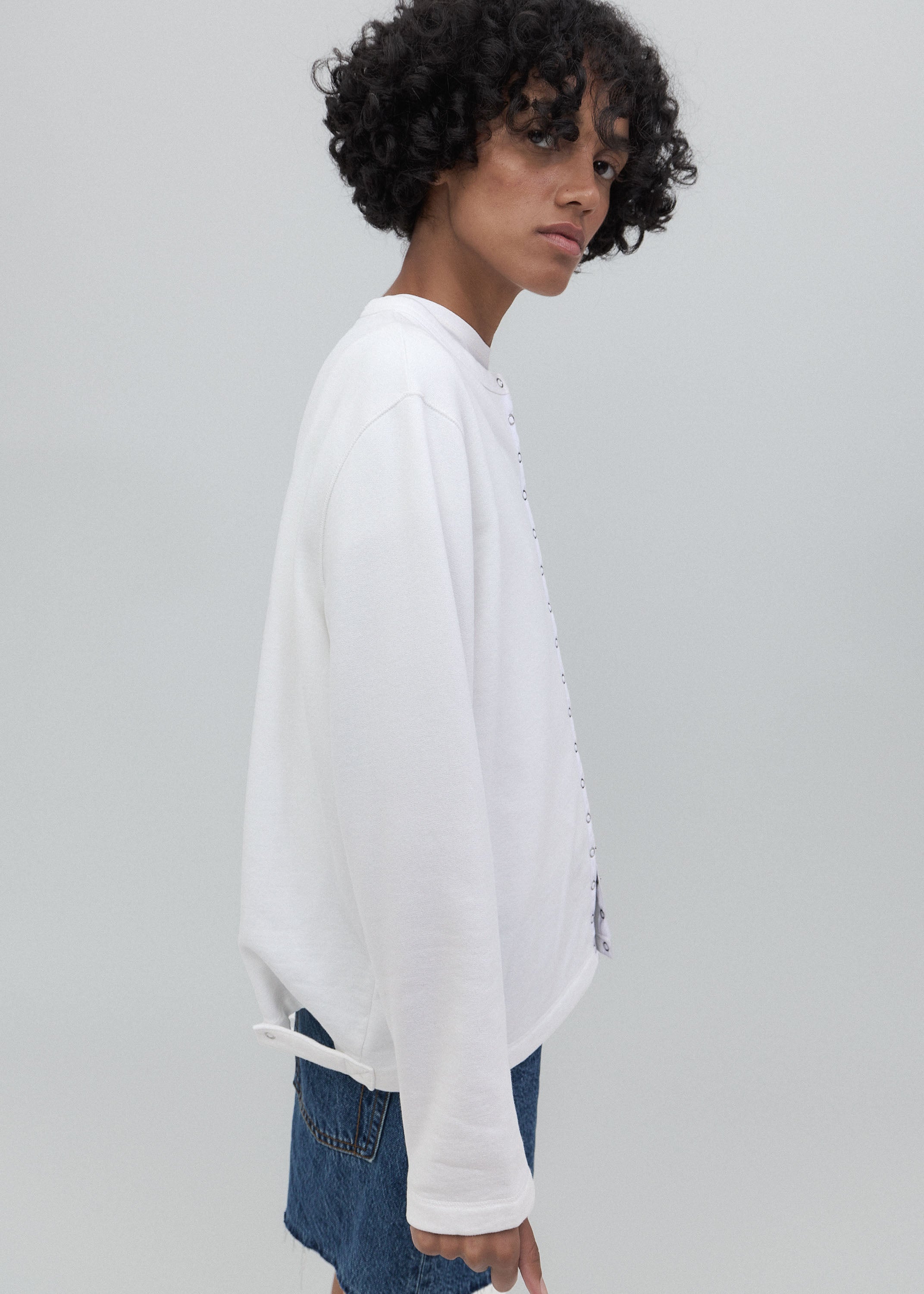 Person wearing a white oversized sweatshirt with a brand logo on a light gray background