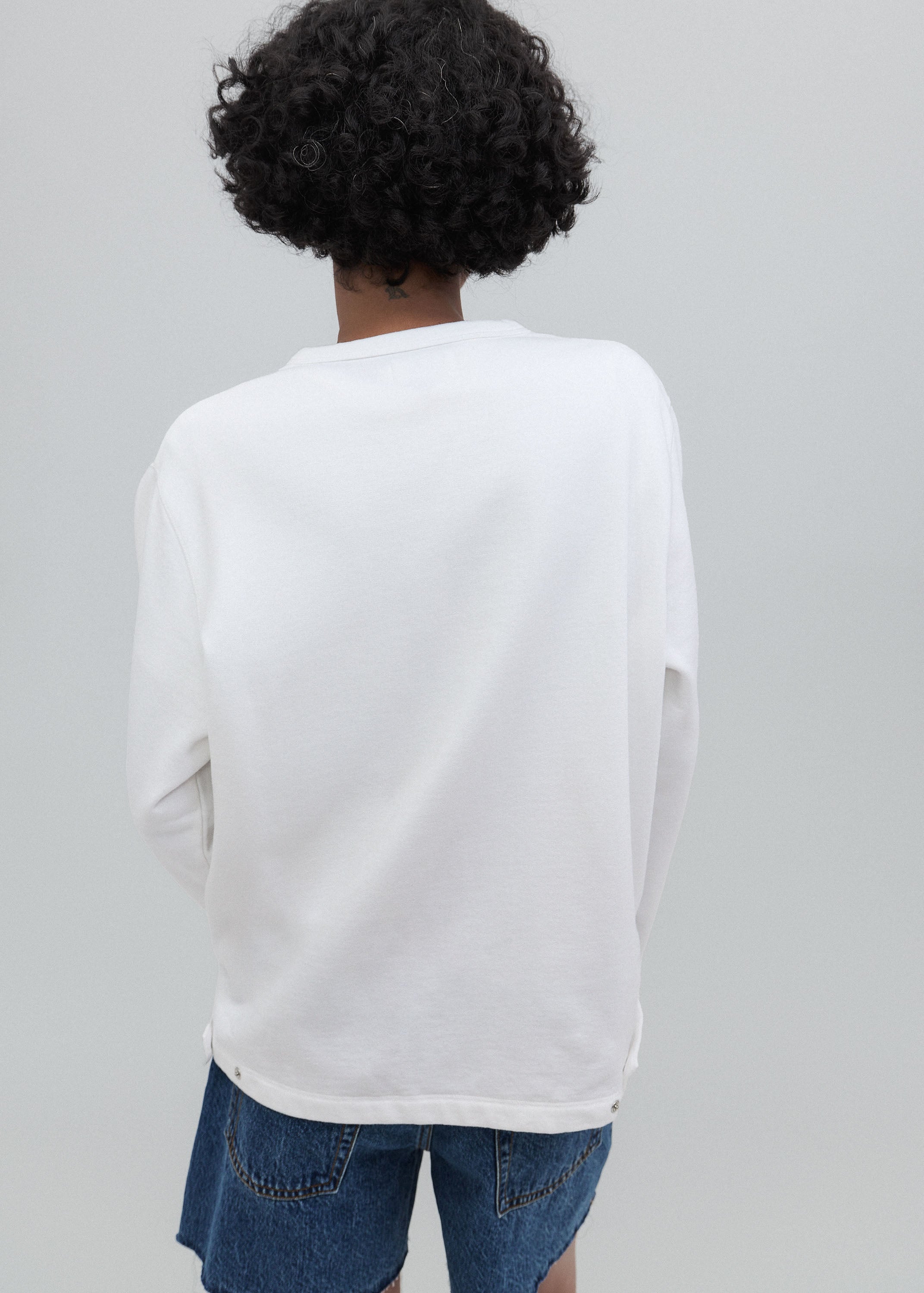 Person wearing a white long-sleeve shirt and blue jeans on a gray background