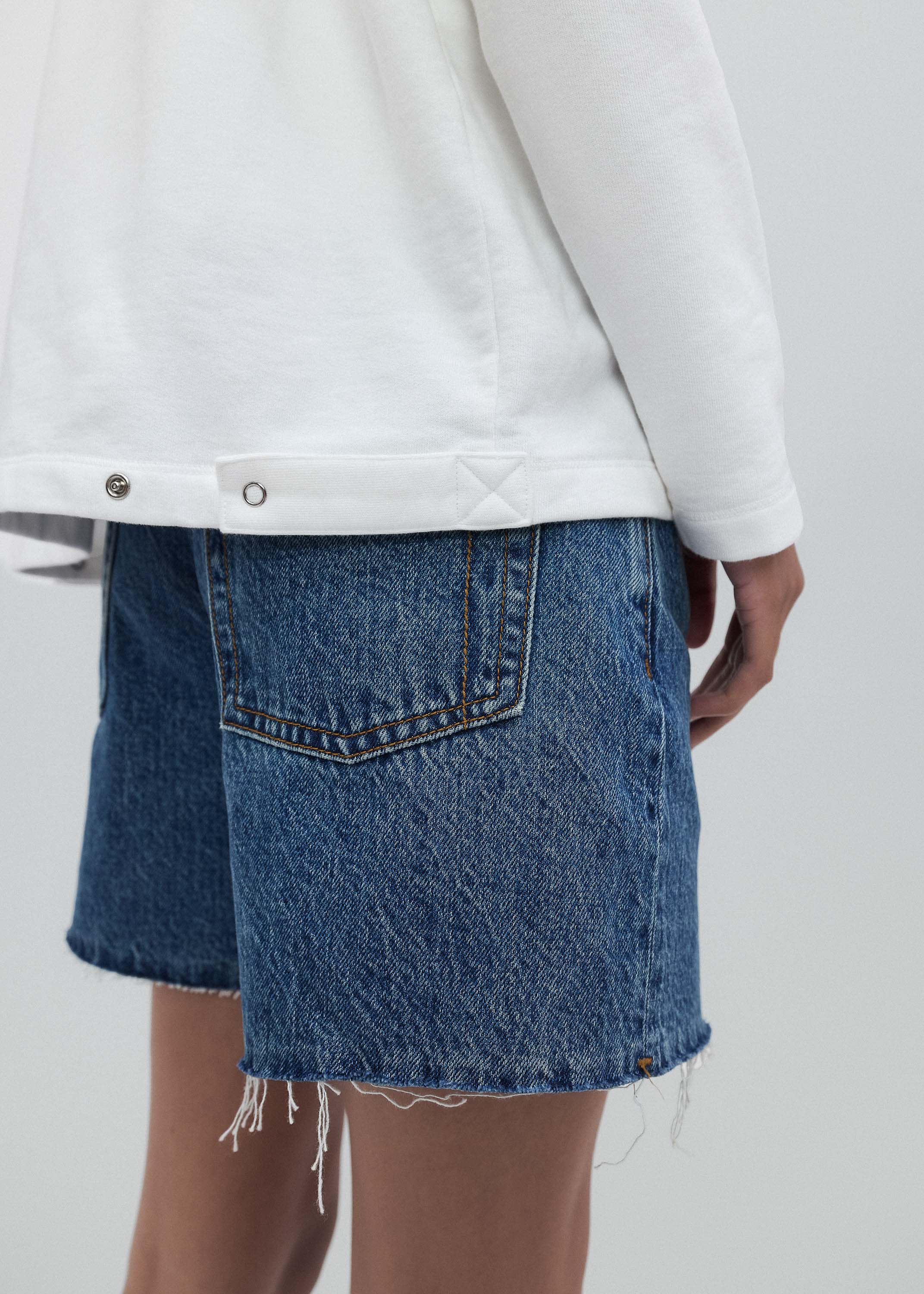 Person wearing a white sweatshirt and blue denim skirt on a plain background
