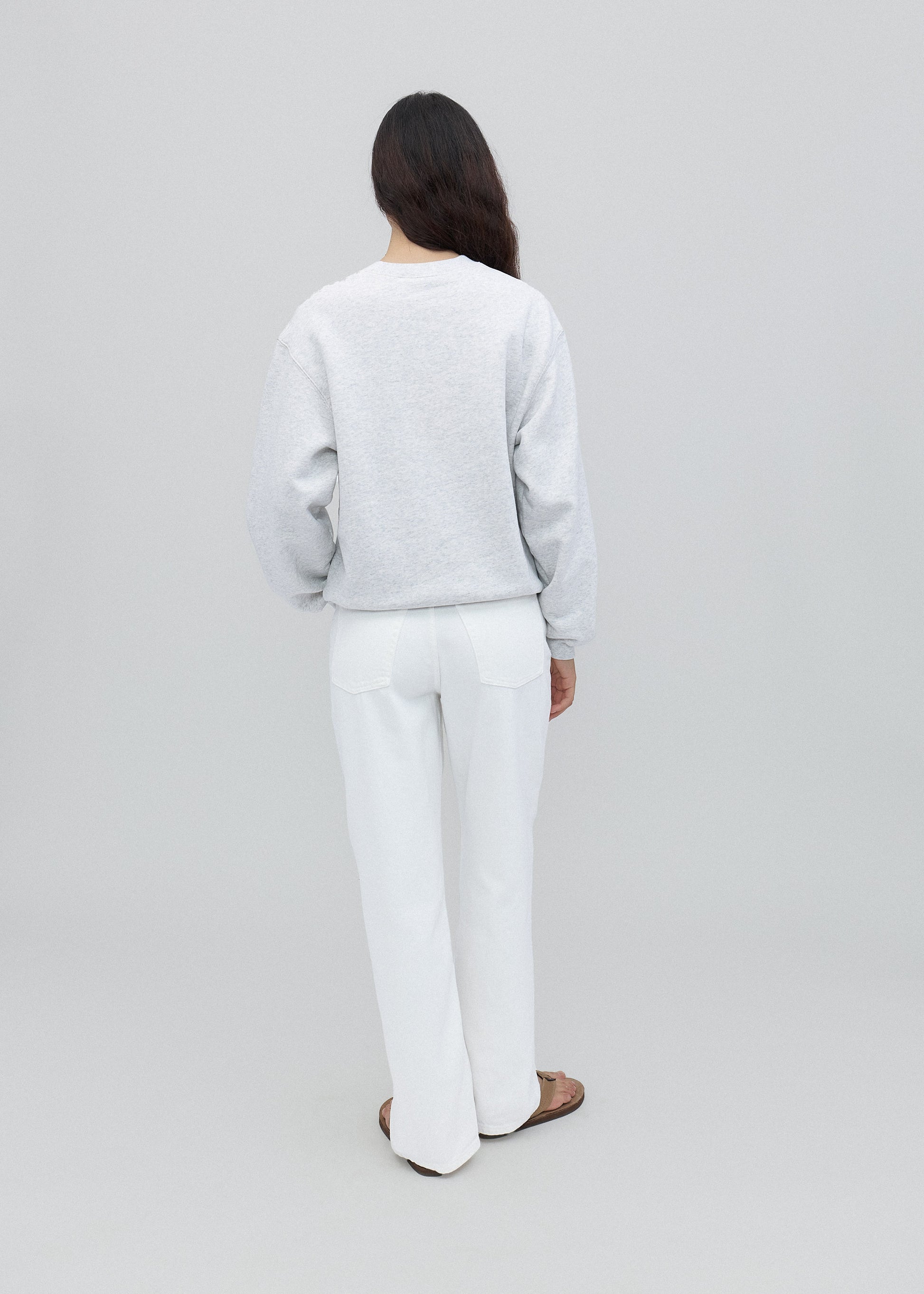 Person wearing a light gray sweater and white pants on a plain background