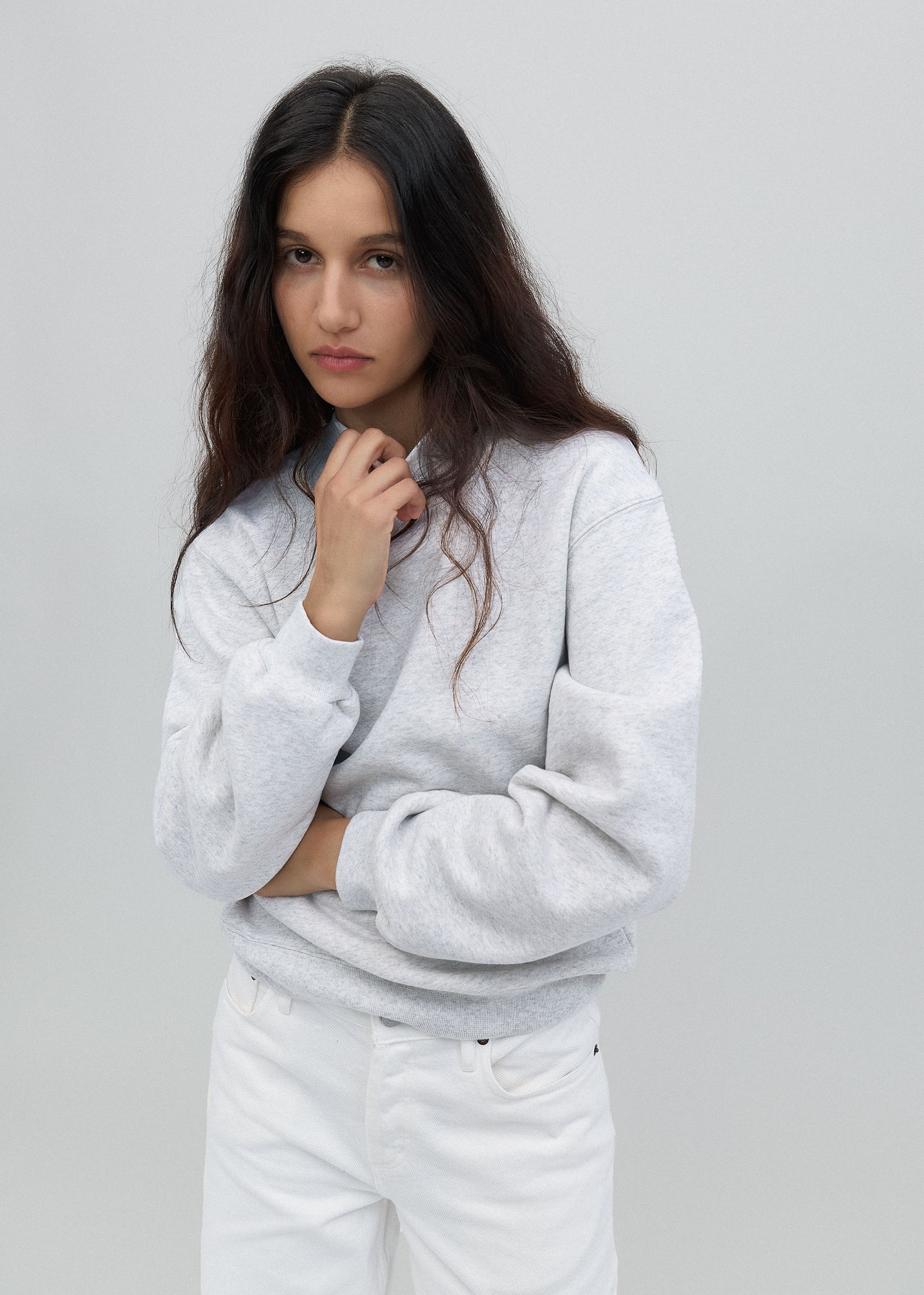 Woman wearing a light gray sweatshirt and white pants against a plain background