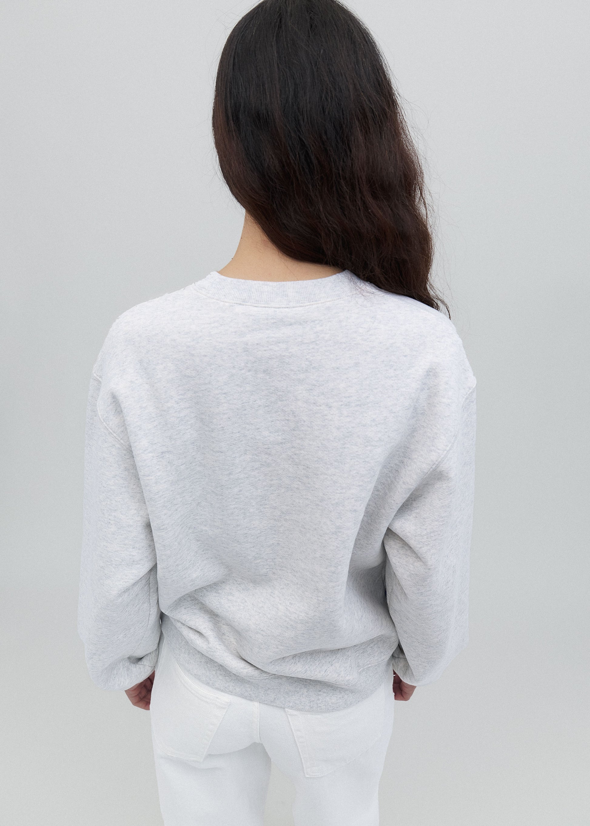 Person wearing a light gray sweater and white pants against a plain background