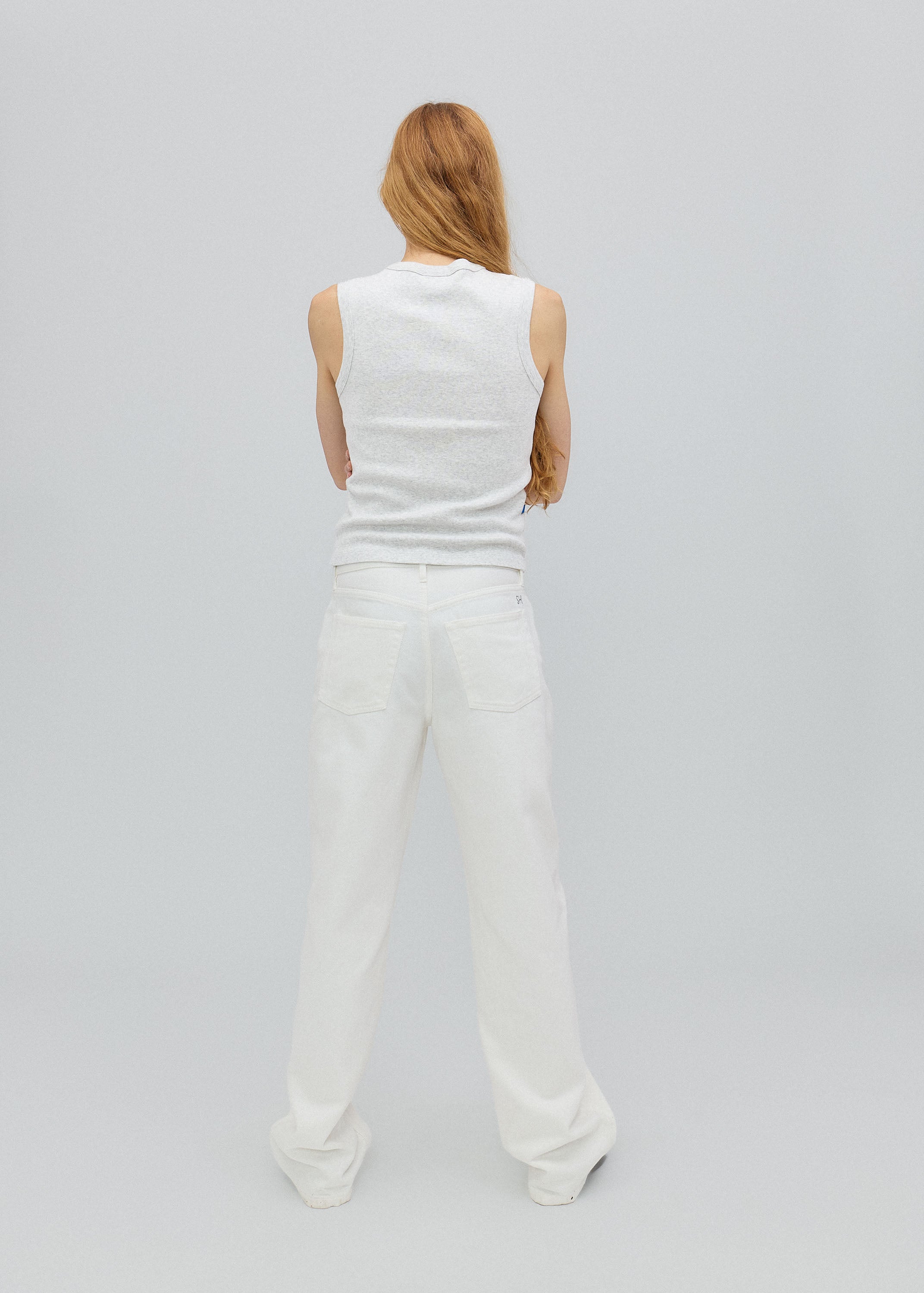 Person wearing a white sleeveless top and pants on a light gray background