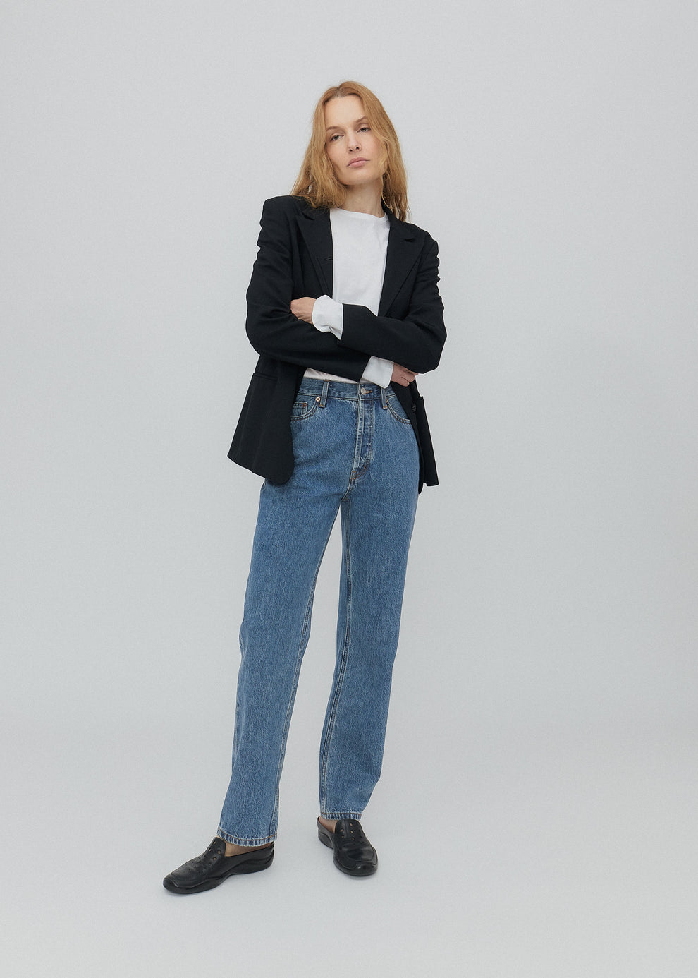 Person wearing a black blazer, white shirt, and blue jeans on a light gray background