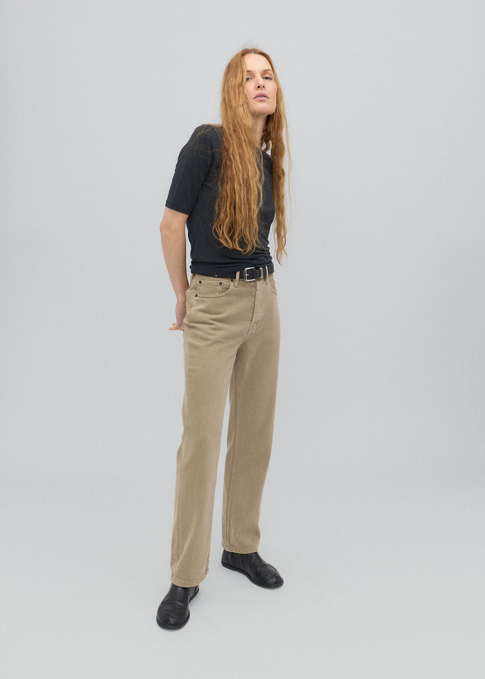 Person wearing a black shirt, beige pants, and black shoes on a light gray background