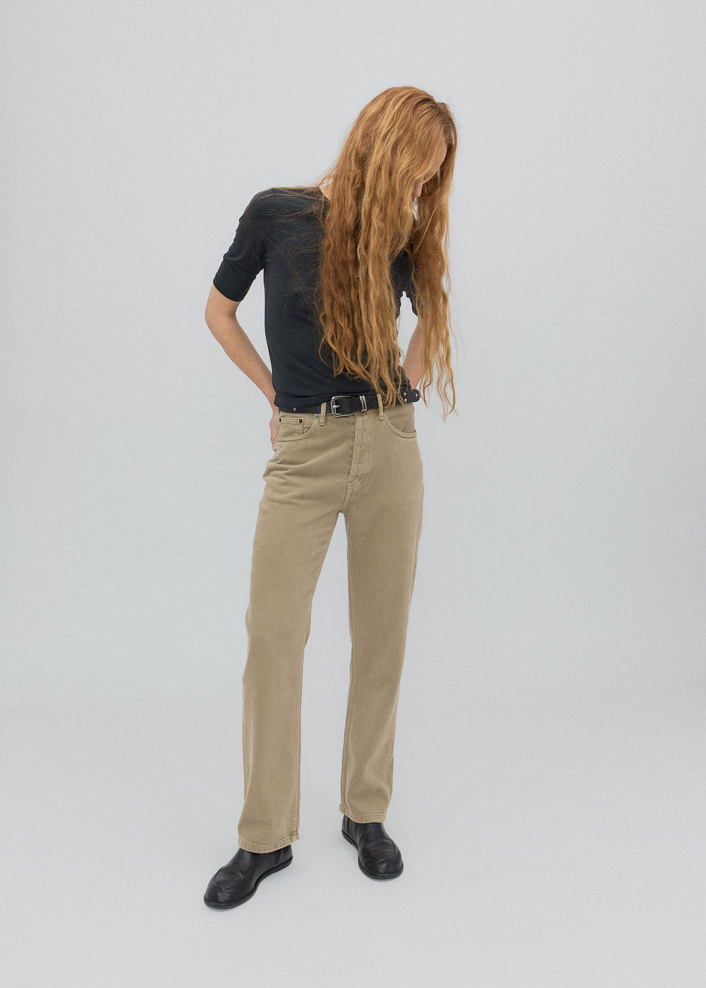 Person wearing a black shirt and beige pants on a plain background