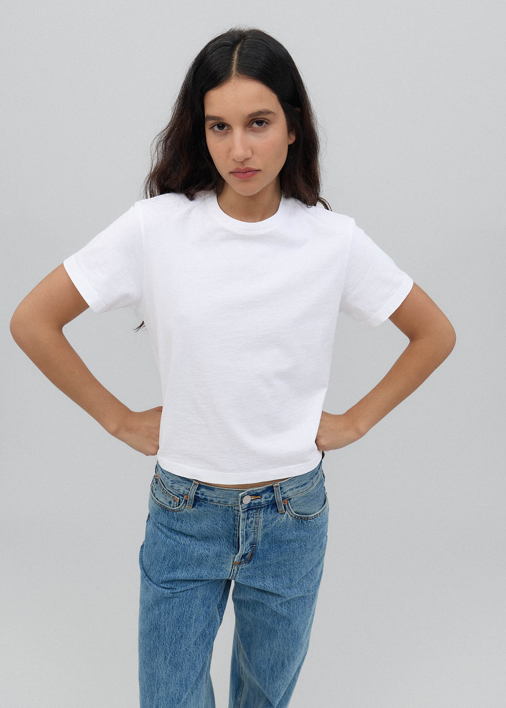 Woman wearing a white t-shirt and blue jeans against a plain background