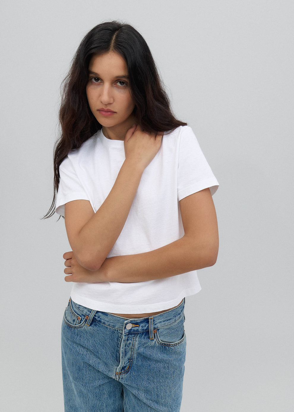 Woman wearing a white t-shirt and blue jeans against a gray background