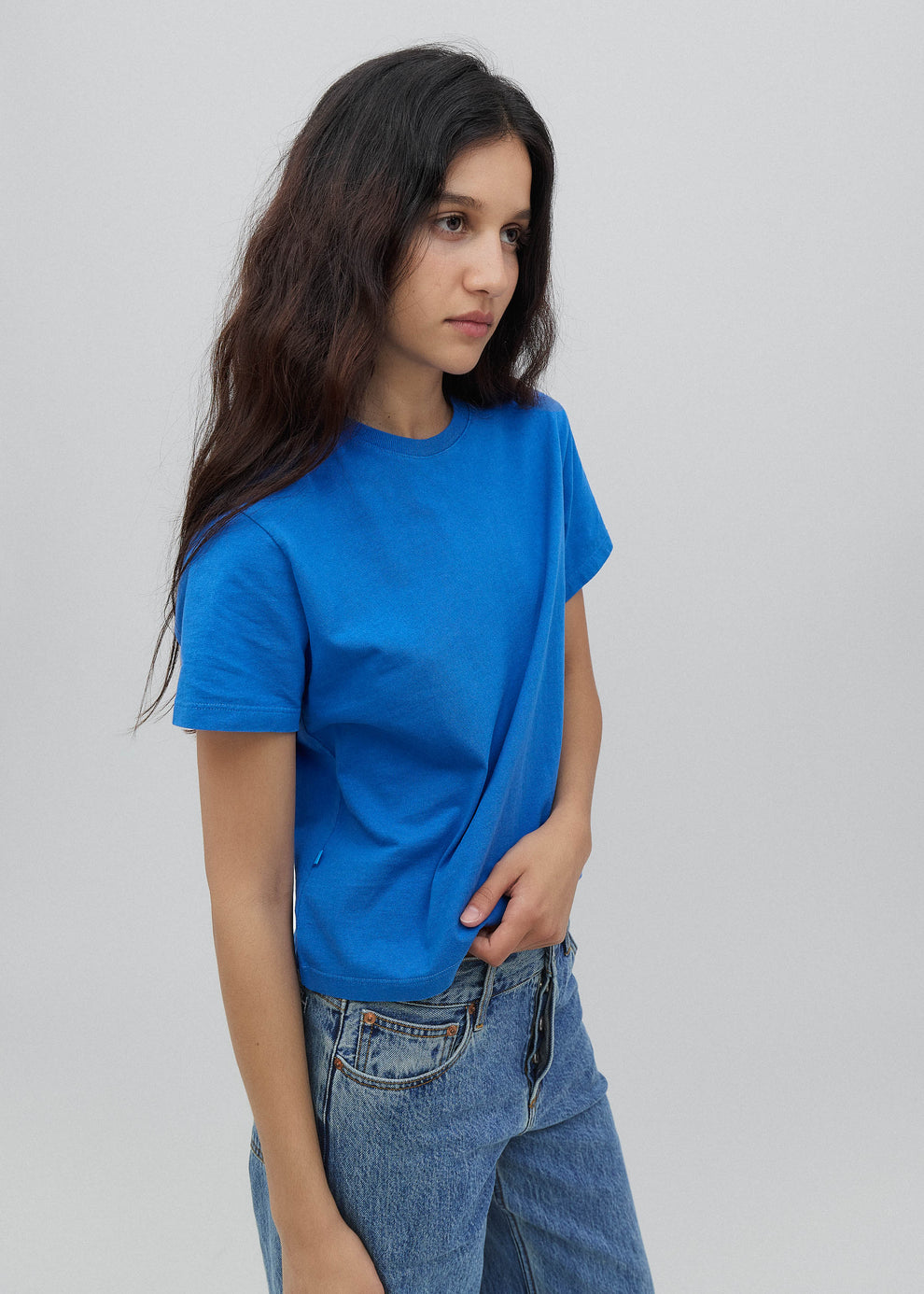 Woman wearing a blue t-shirt and jeans against a plain background