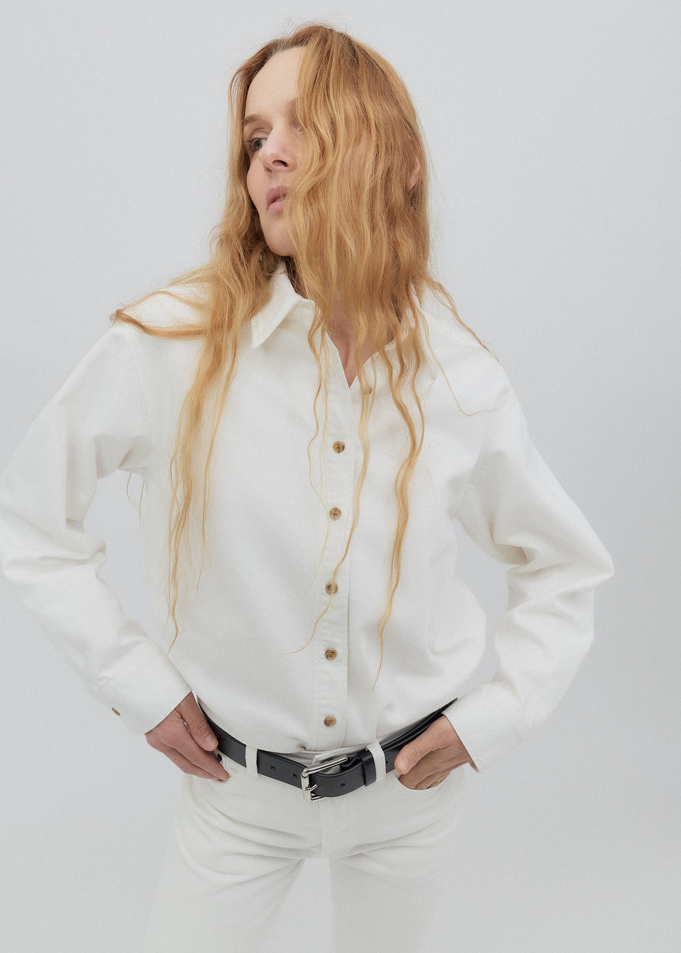 Person wearing a white shirt with a black belt against a plain background