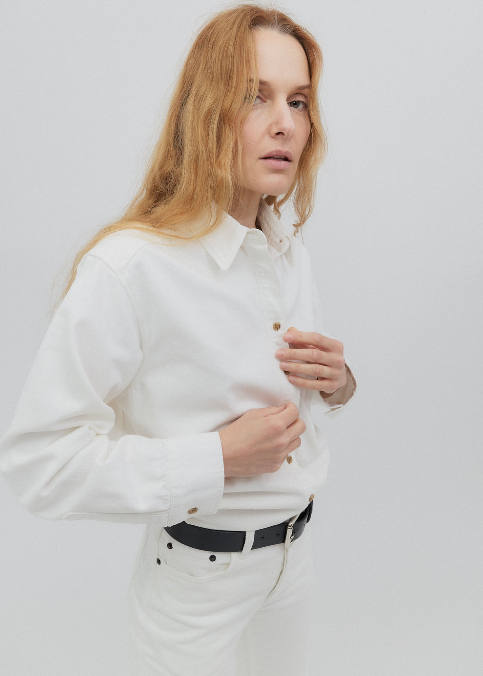 Woman wearing a white shirt with a black belt against a plain background