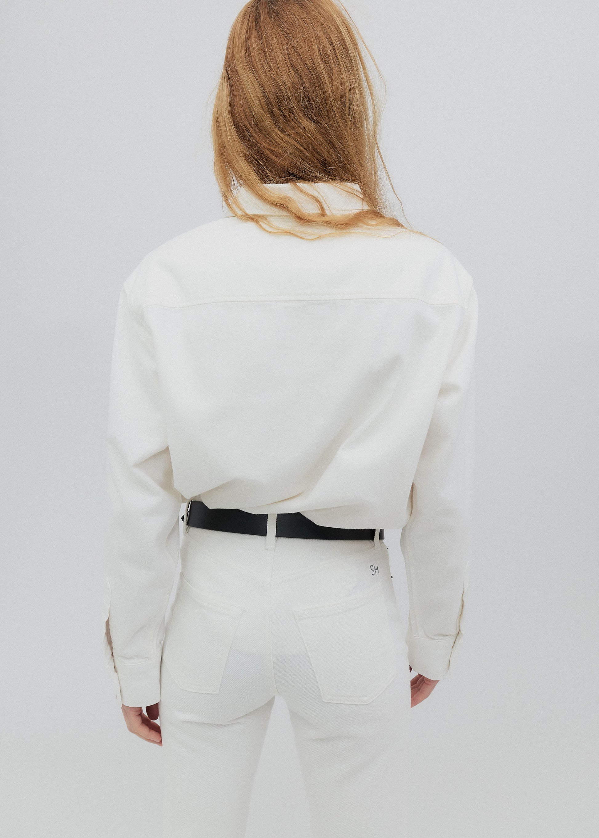 Person wearing a white outfit with a black belt on a plain background