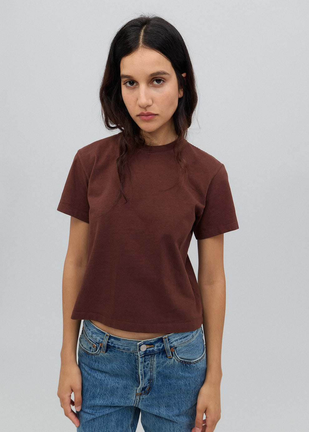 Woman wearing a brown t-shirt and blue jeans against a plain background