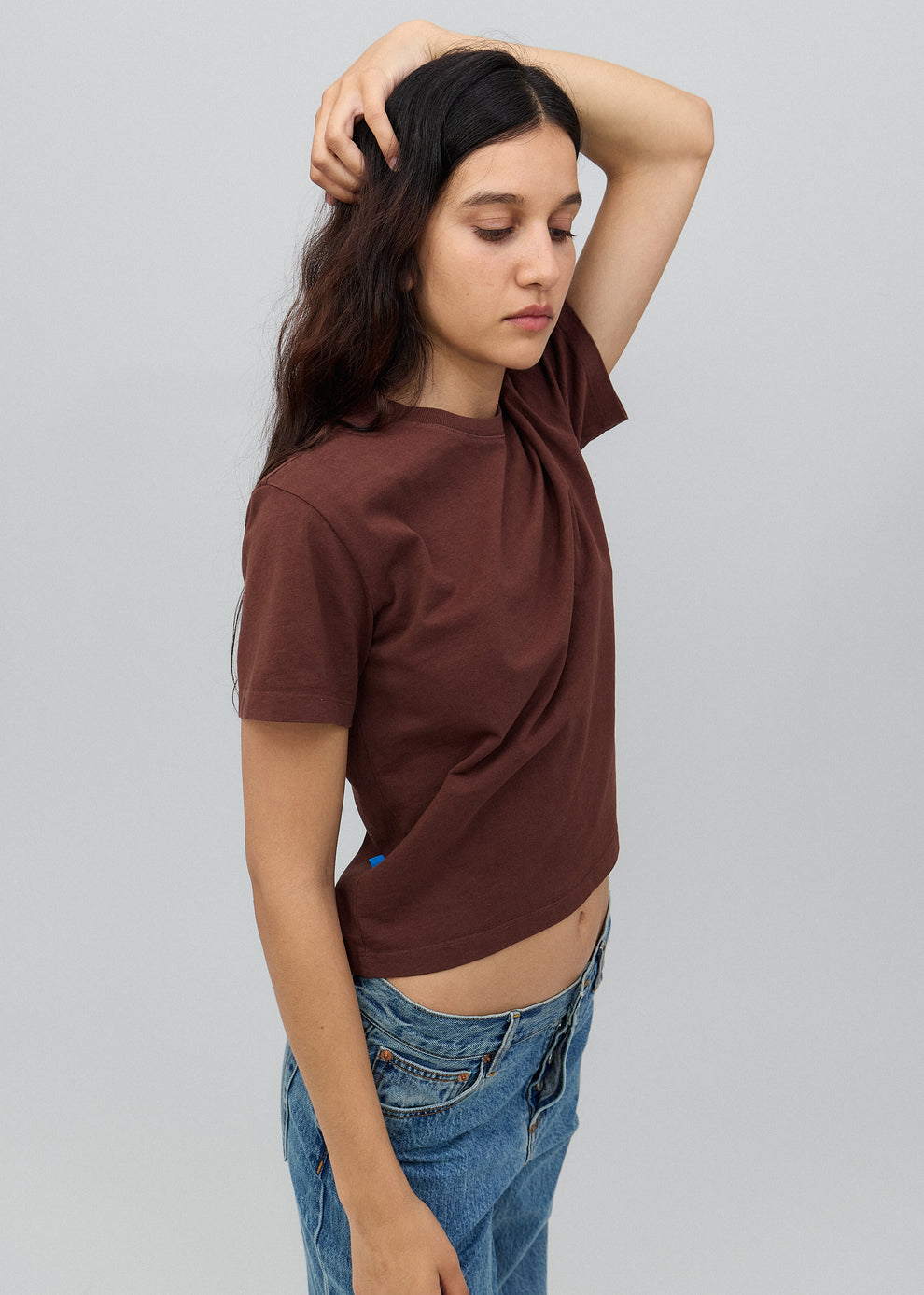 Person wearing a brown t-shirt and blue jeans against a plain background