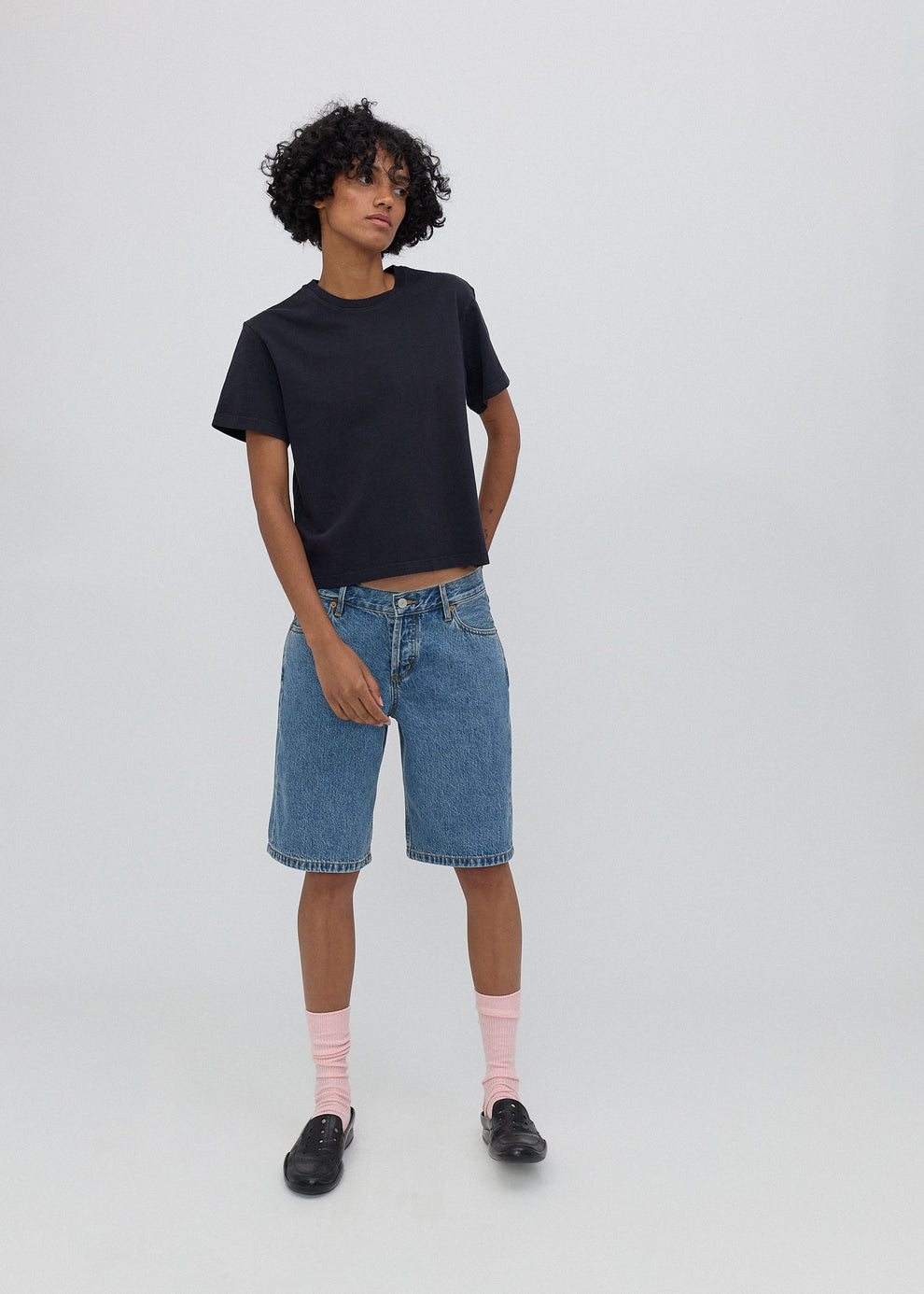 Person wearing a black t-shirt and blue denim shorts on a white background