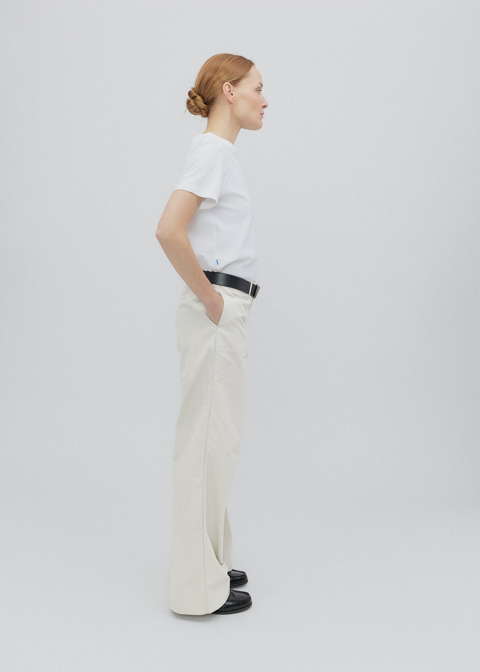 Person wearing a white shirt and beige pants on a plain background