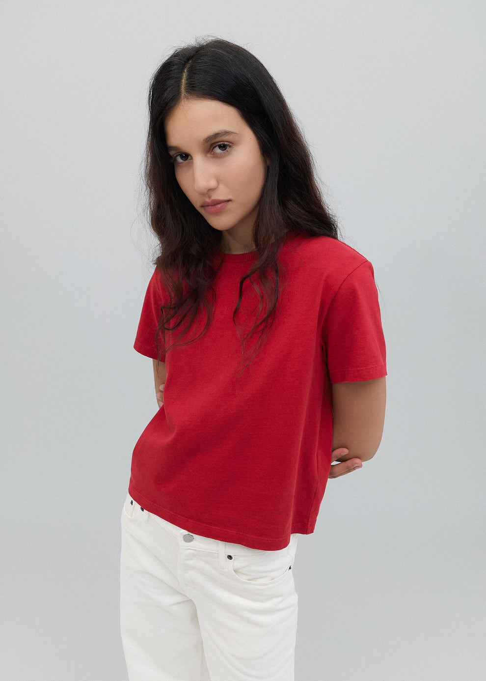 Woman wearing a red t-shirt and white pants against a gray background