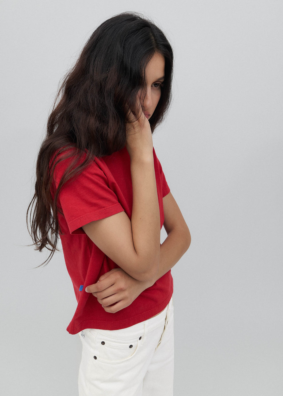 Woman wearing a red shirt and white pants against a gray background