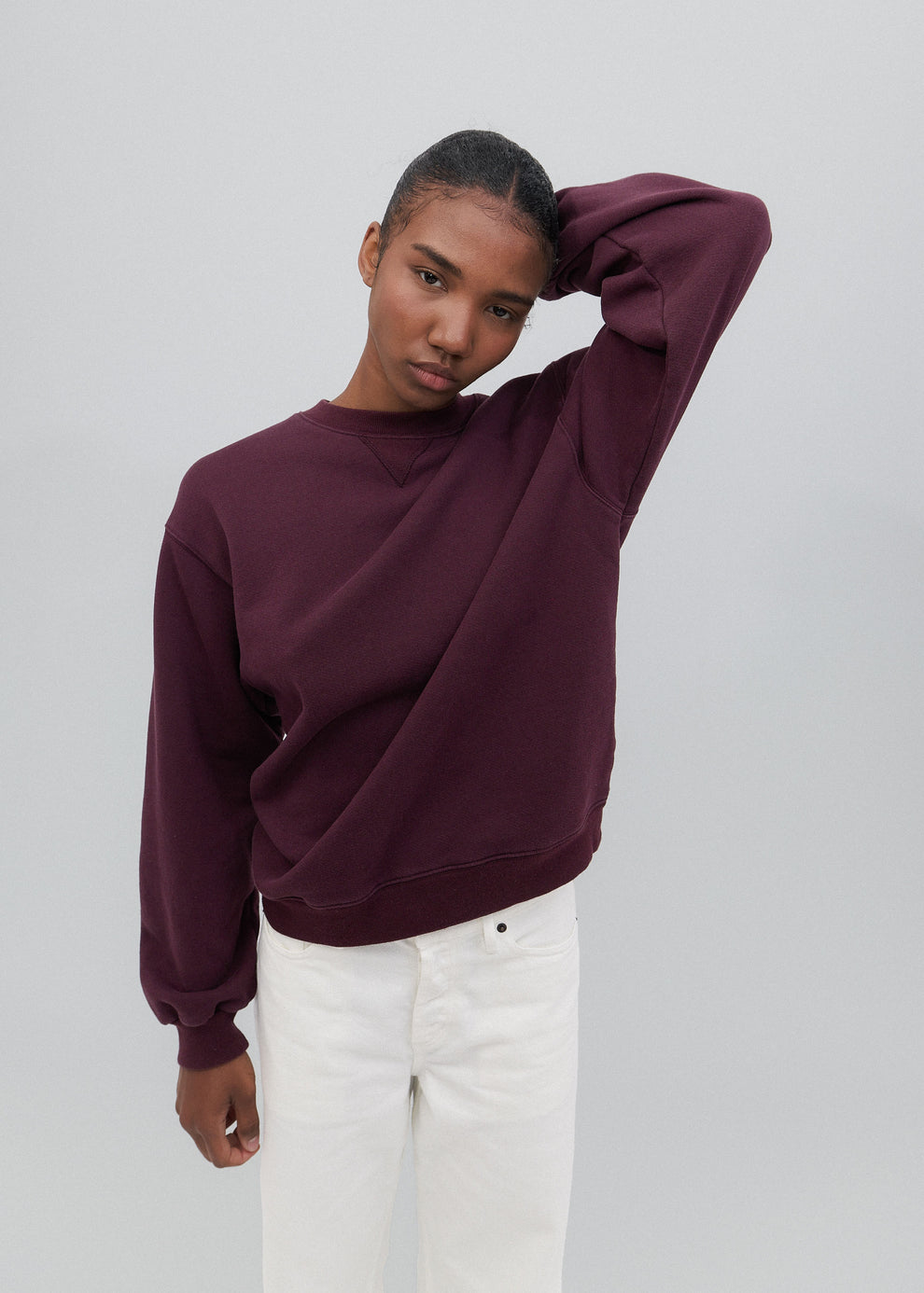 Person wearing a burgundy sweater and white pants on a plain background