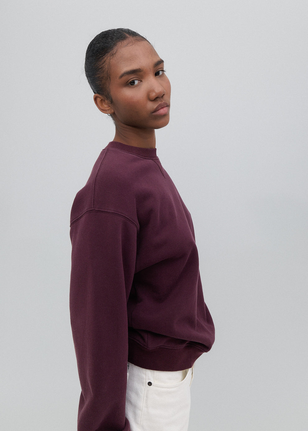 Person wearing a maroon sweatshirt and white pants on a plain background