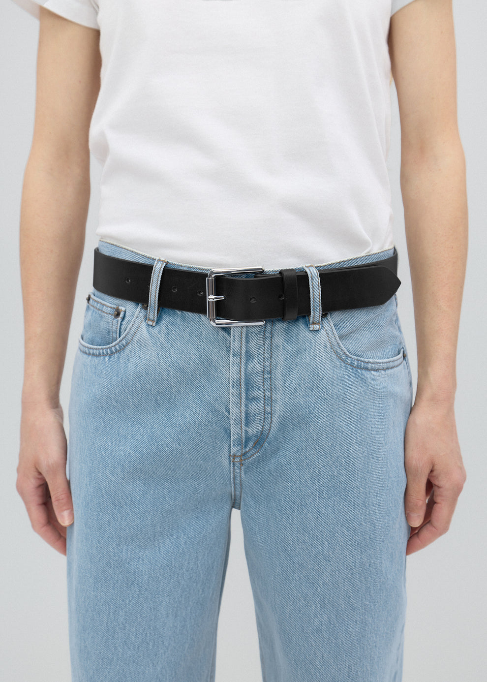 Person wearing a white t-shirt and light blue jeans with a black belt on a plain background
