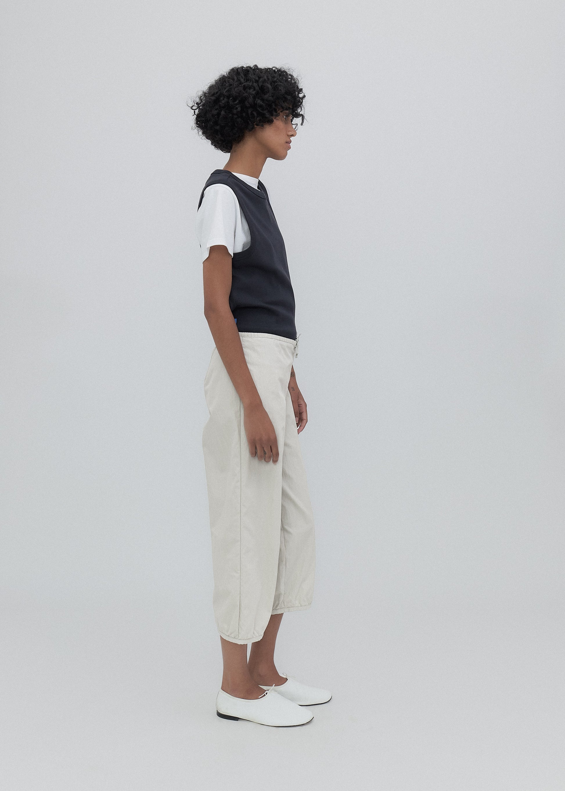 Person wearing a black sleeveless top and white pants on a plain background