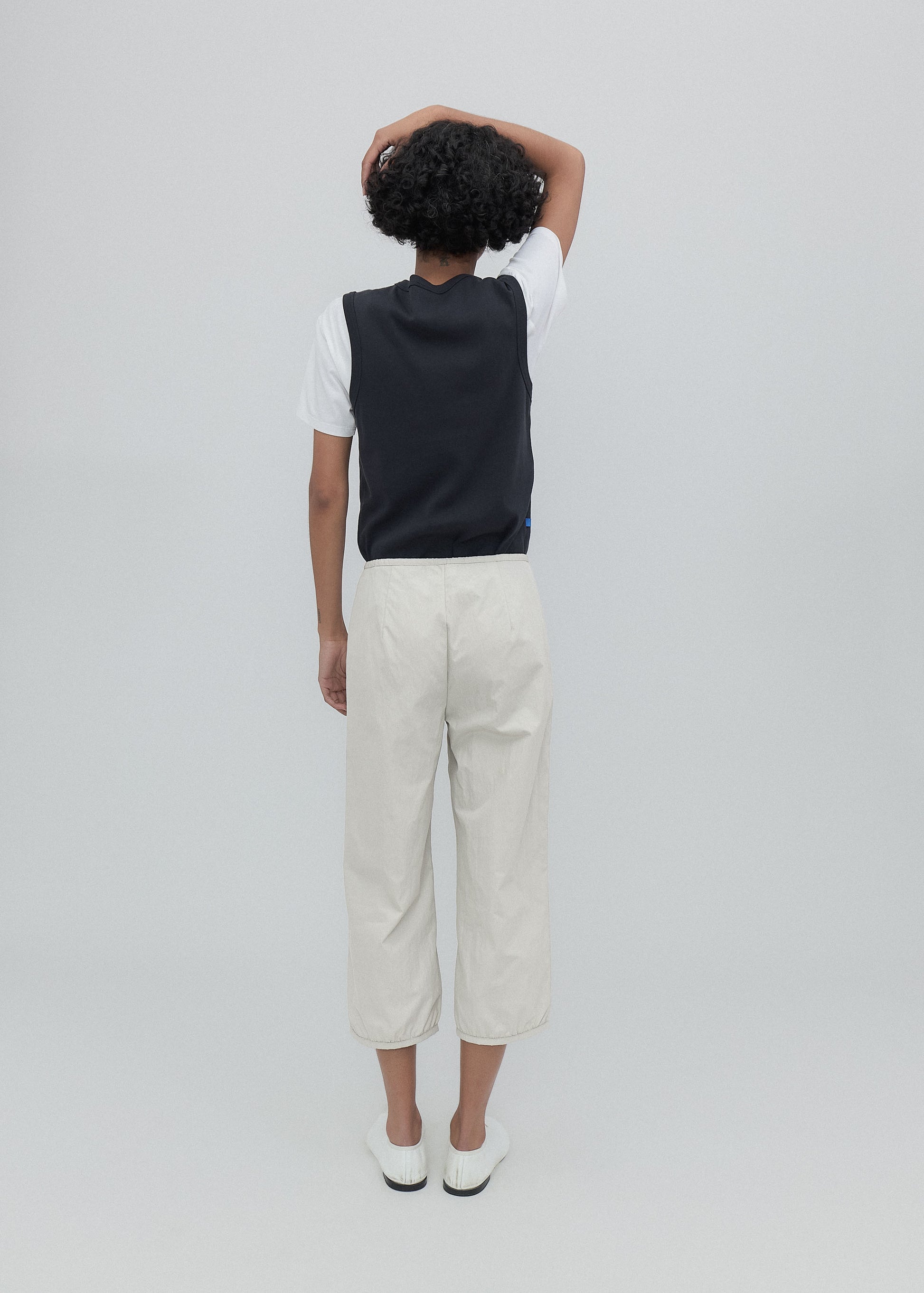 Person wearing a black vest over a white shirt with beige pants on a light gray background