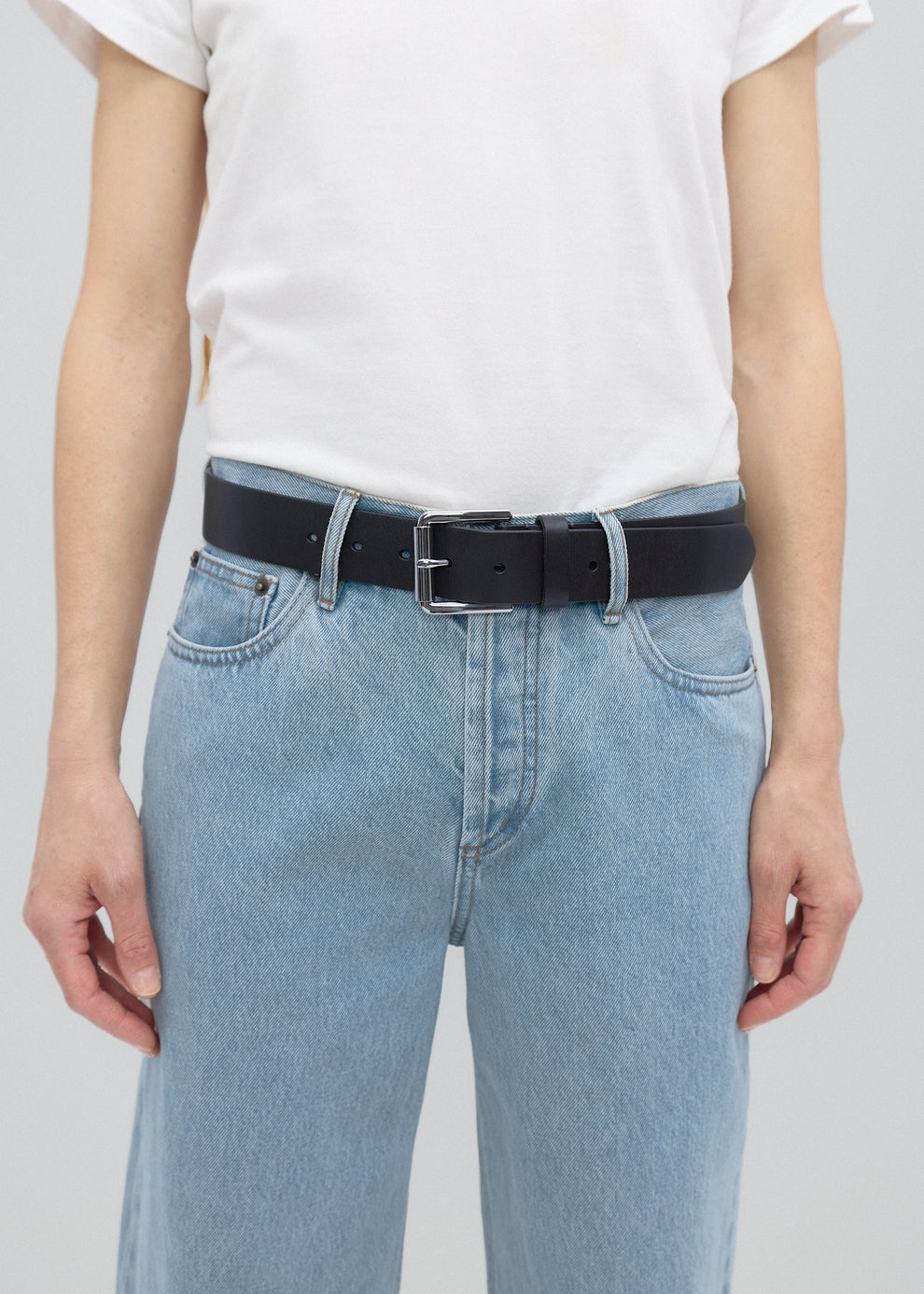 Person wearing light blue jeans and a black belt on a plain background