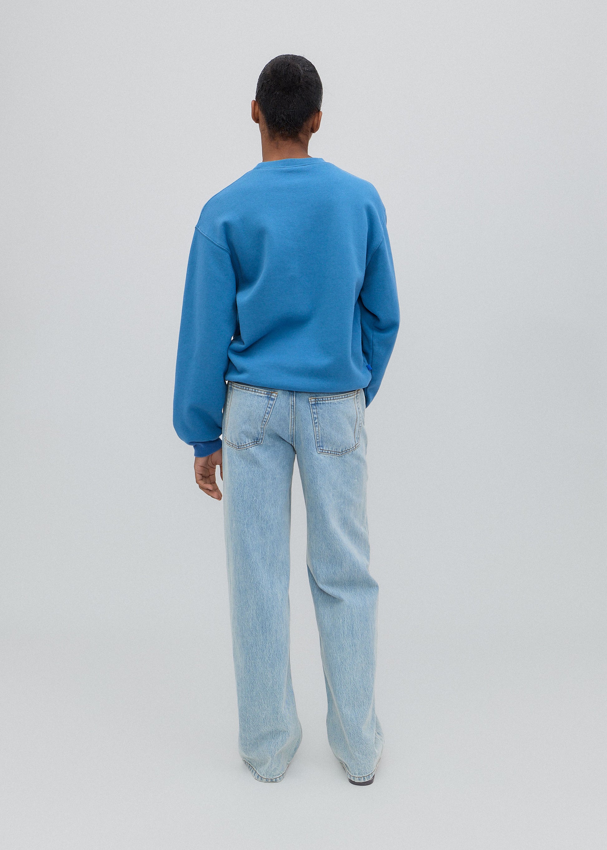 Person wearing a blue sweater and light blue jeans on a plain background