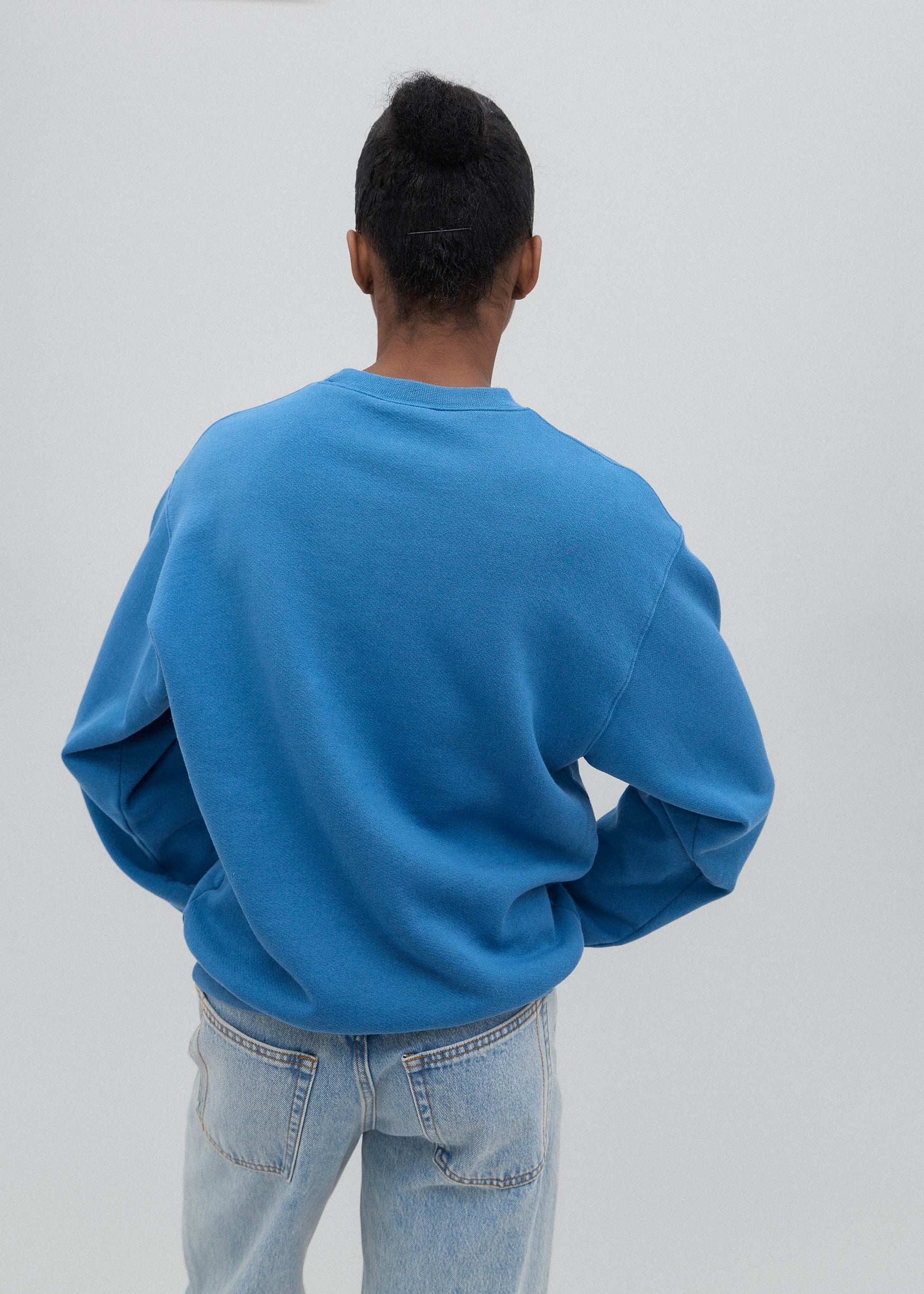 Person wearing a blue sweatshirt and light blue jeans against a white background