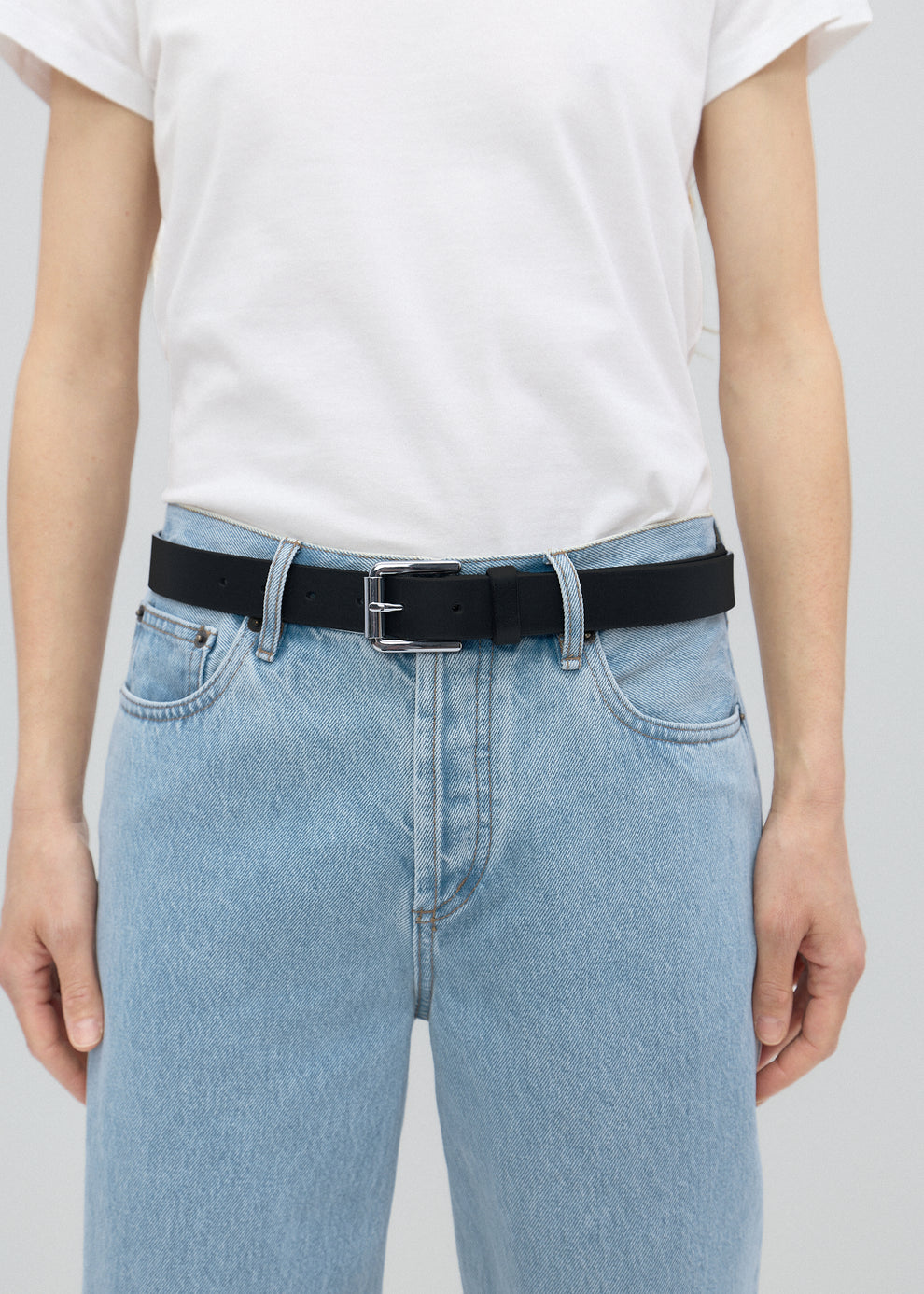 Person wearing light blue jeans with a black belt on a plain background